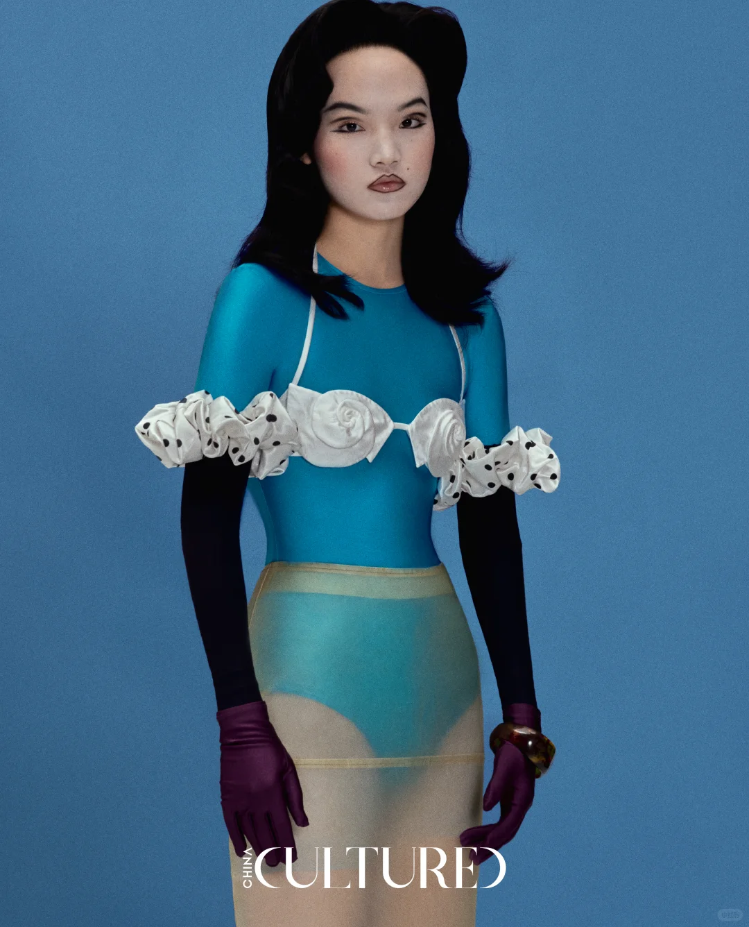 A model in a blue bodysuit crossed by a white sculptural floral frame, translucent lower layer and long gloves