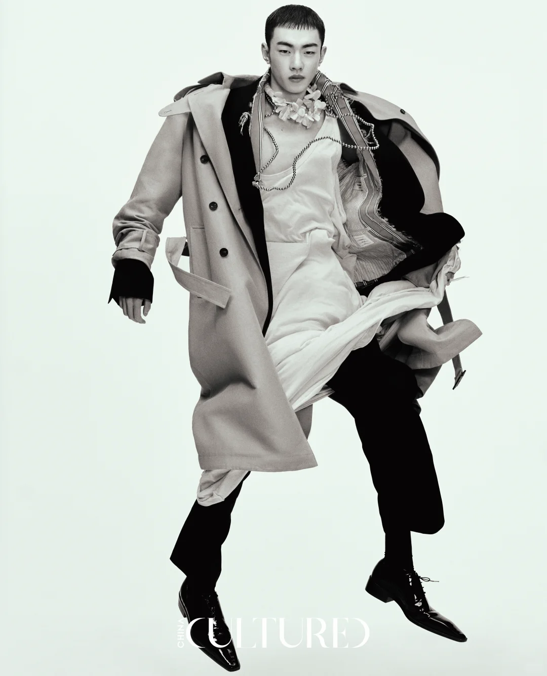 A monochrome editorial look combining a deconstructed trench, displaced tailoring, chains and layered fabric in motion