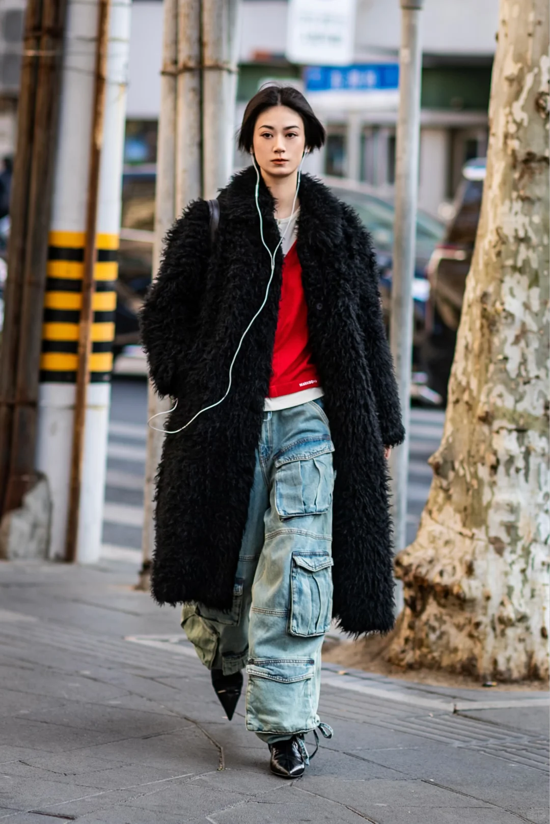 A woman walking on a Shanghai pavement in a black textured coat, red top and wide cargo jeans