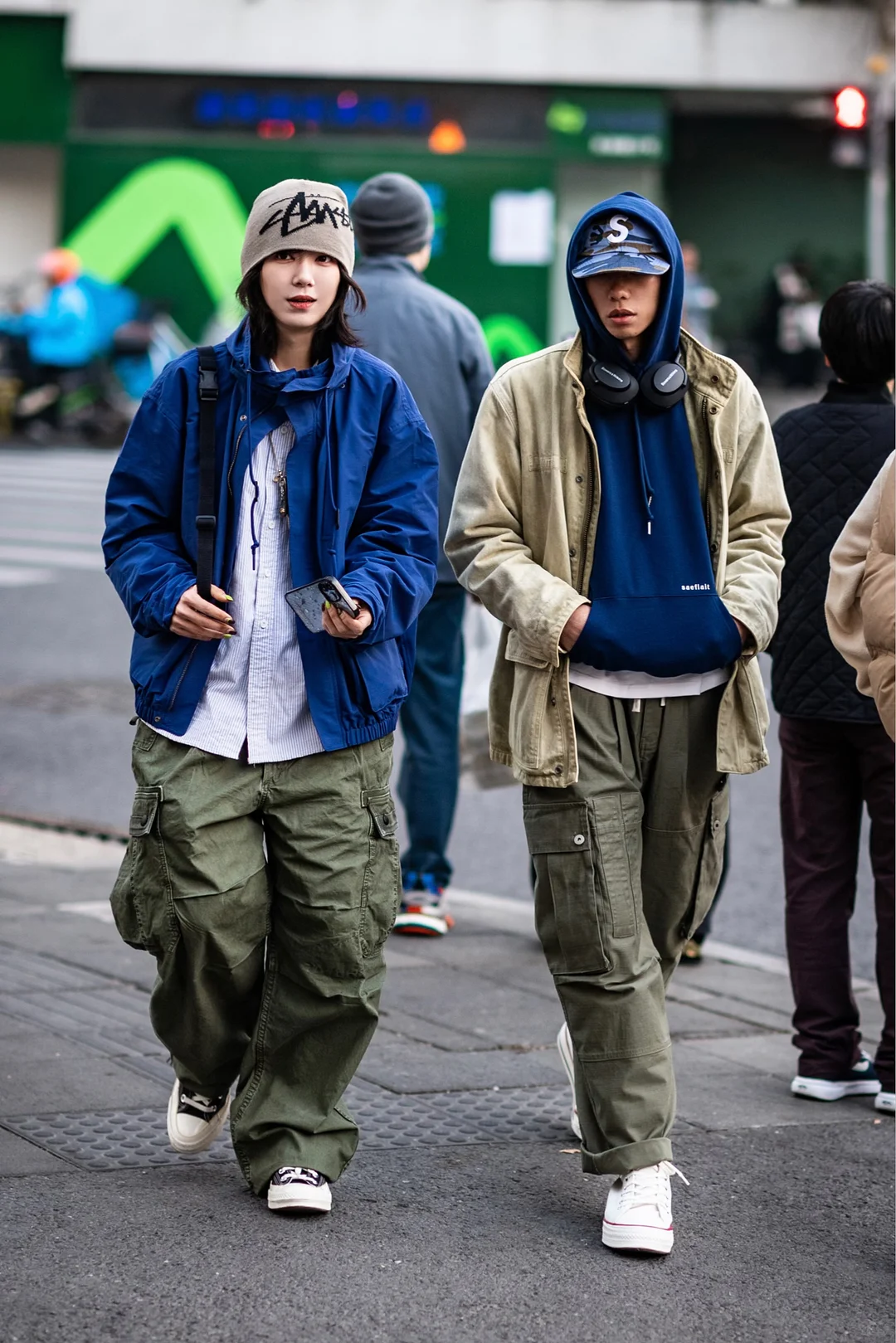 Two pedestrians in Shanghai wearing layered blue, khaki and olive utility pieces with wide cargo trousers