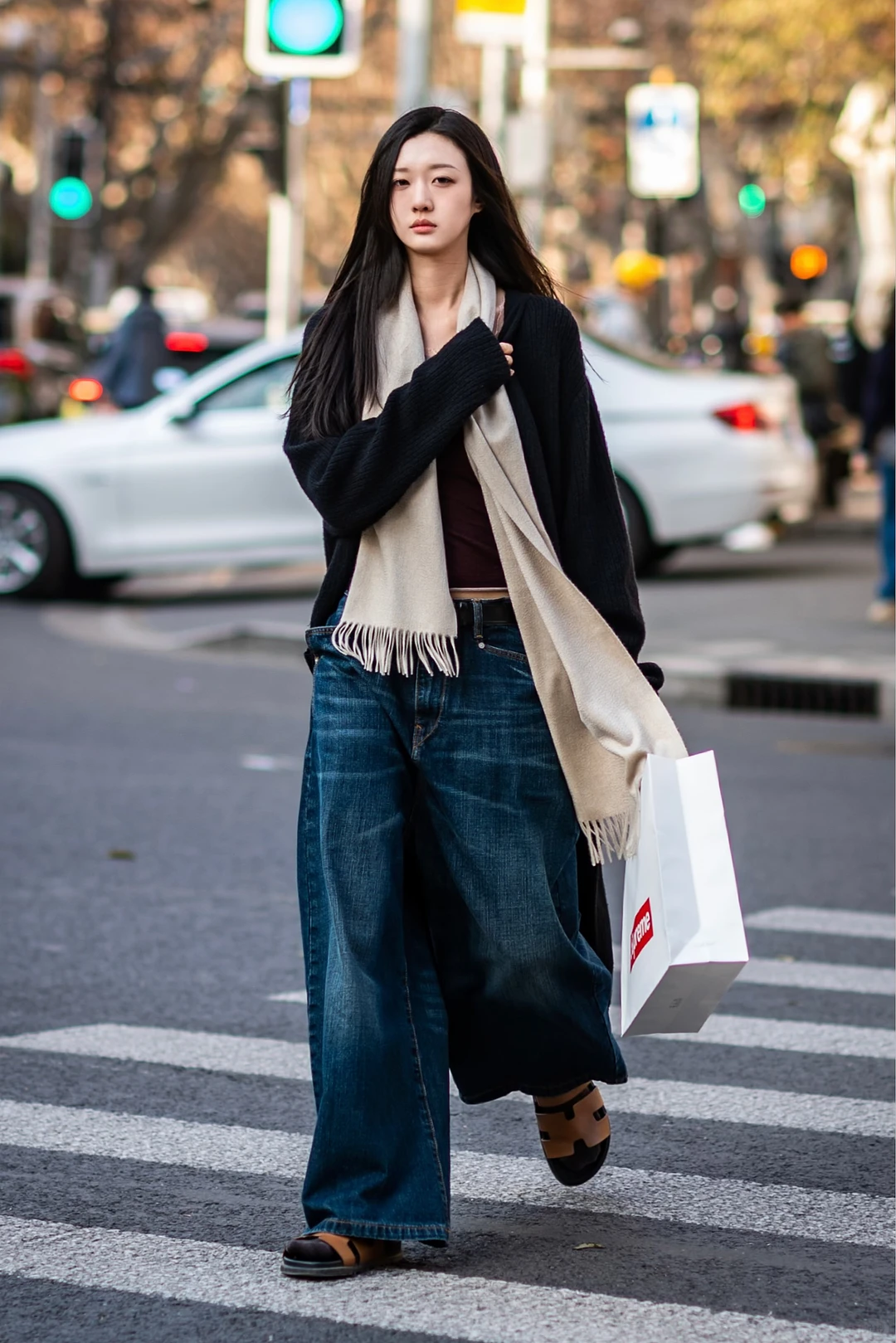A woman crossing a Shanghai street in a black knit, long scarf, dark wide denim and practical flat shoes