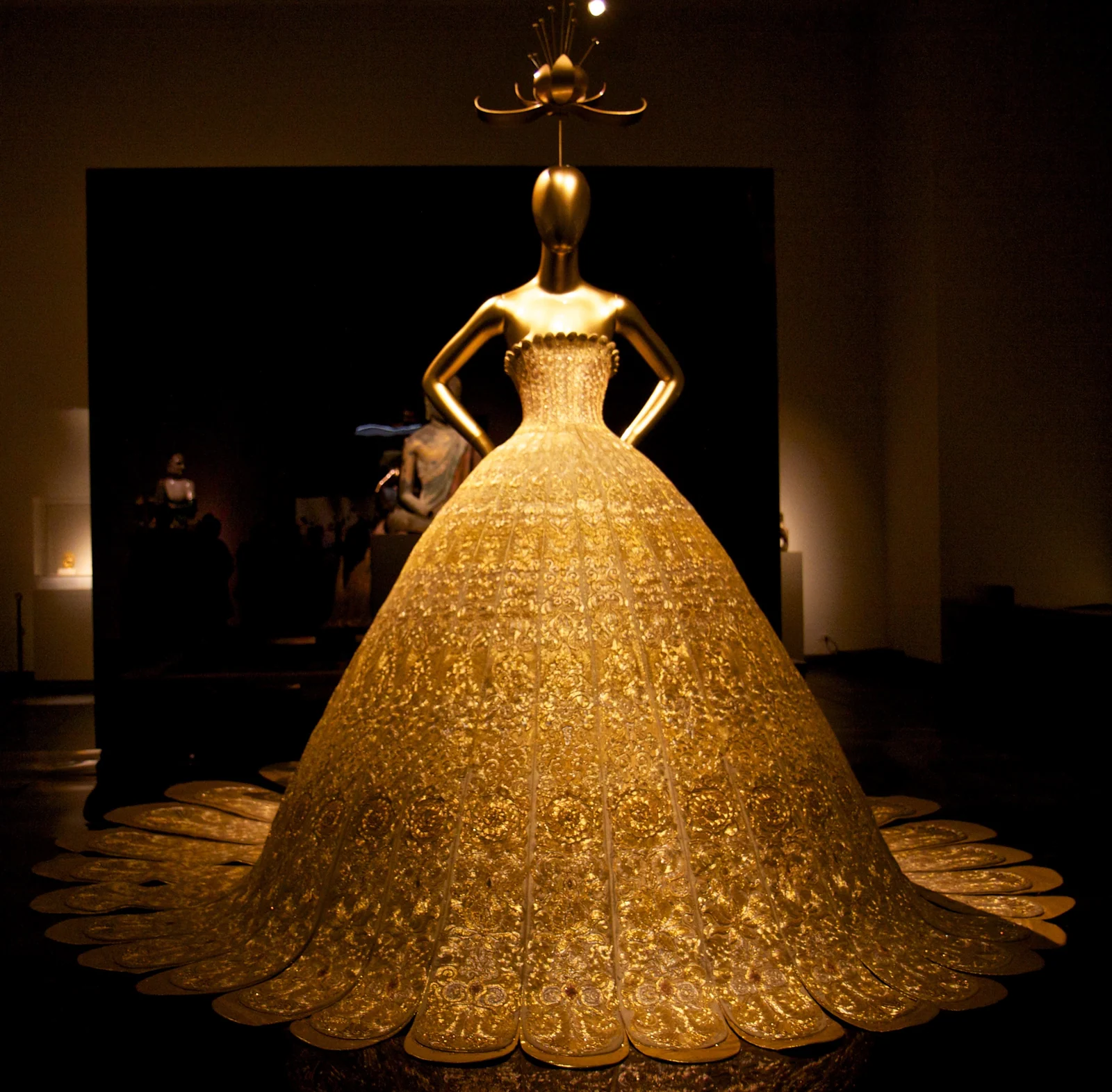 A monumental gold Guo Pei couture gown displayed in a museum gallery