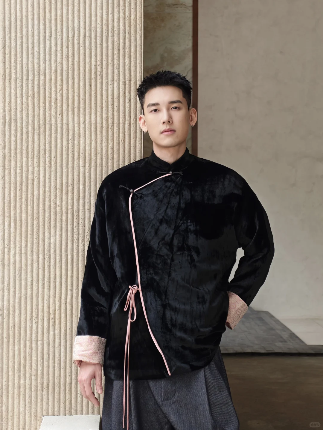 A model wearing a black velvet jacket with asymmetric pink-edged knot fastening and wide dark trousers