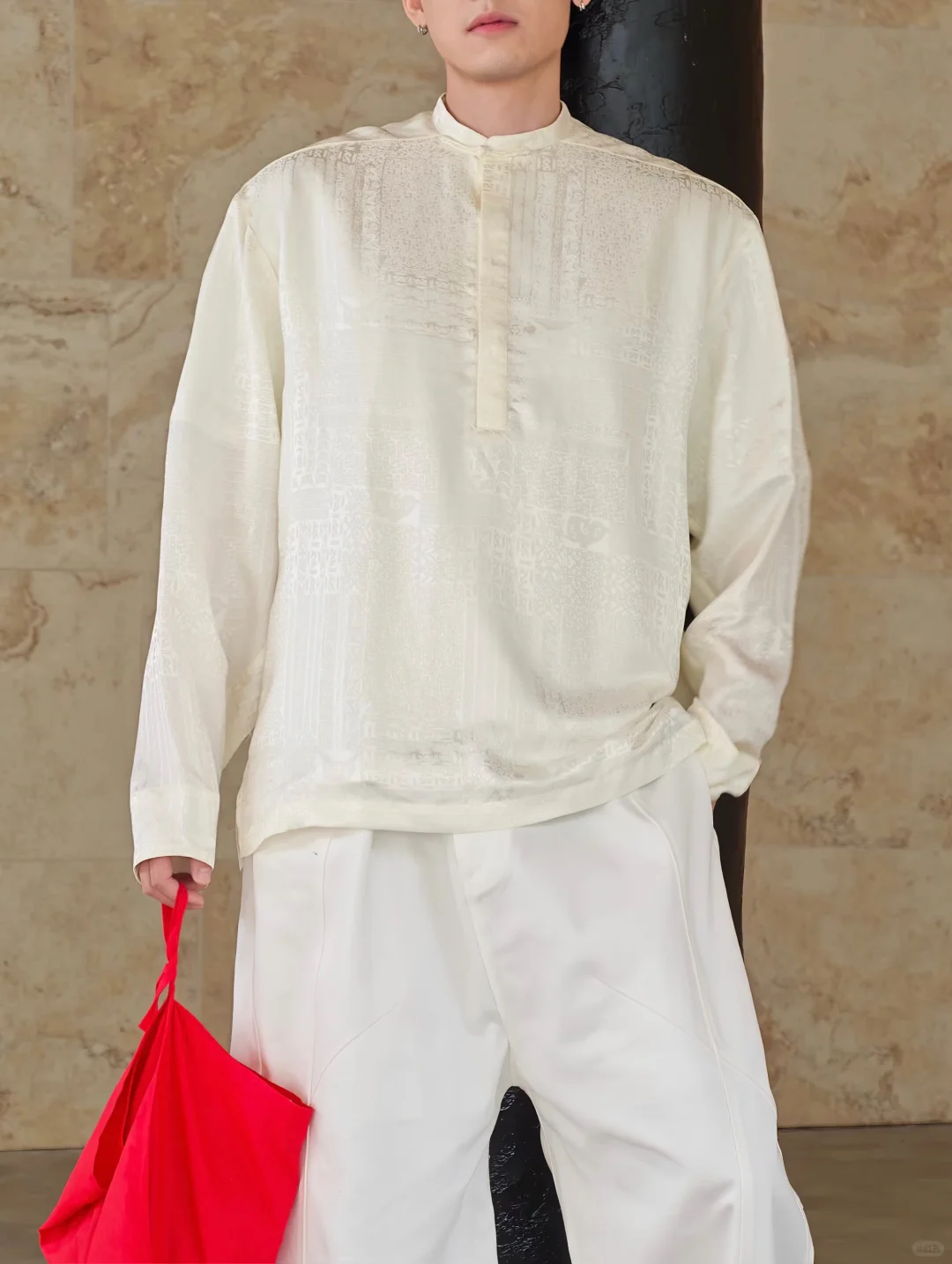 A close view of an ivory woven pullover and wide white trousers interrupted by a bright red fabric tote