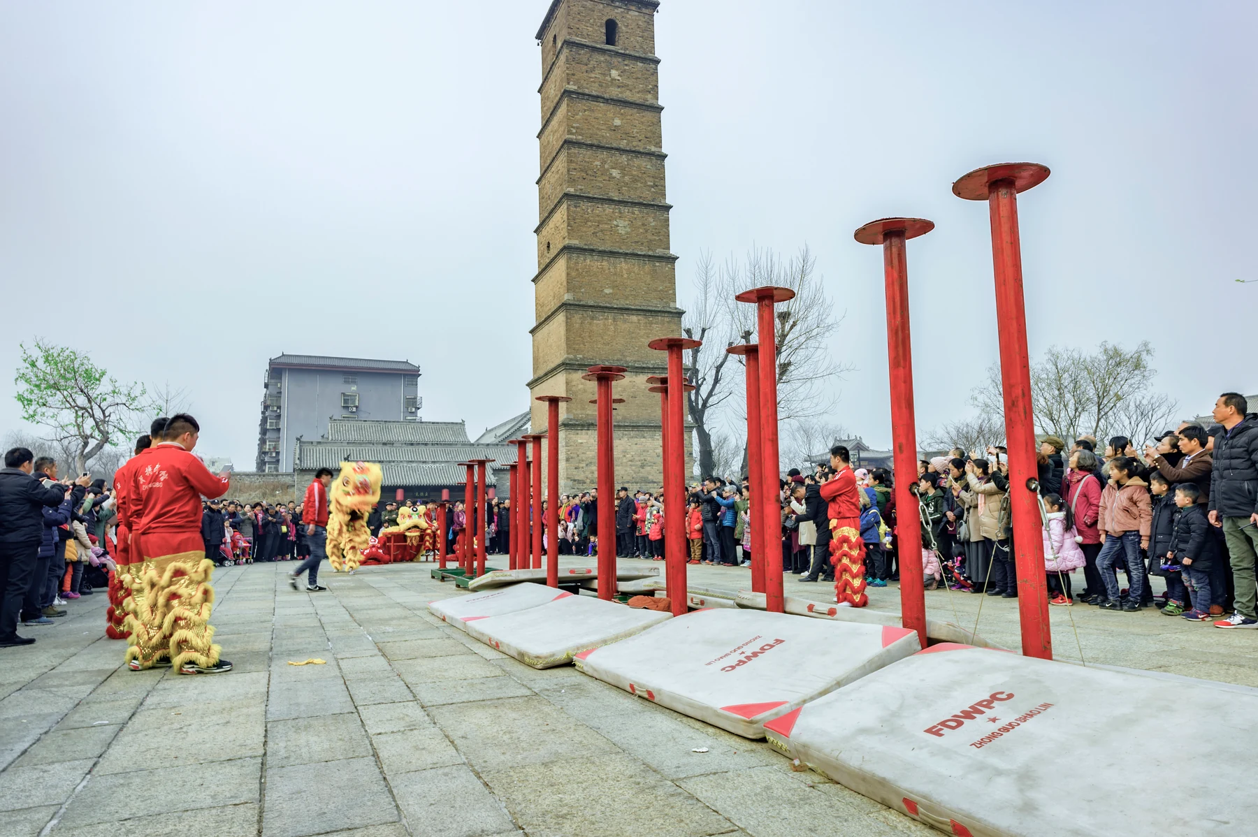 A real Luoyang lion-dance performance surrounded by families beside an old brick pagoda