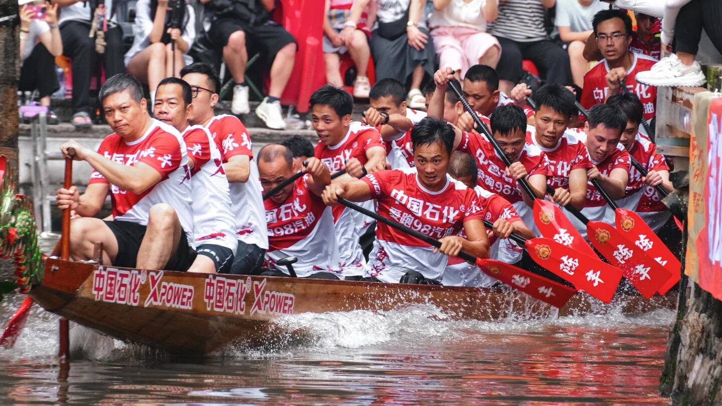 A real dragon-boat crew turning through a narrow spectator-lined waterway in Diejiao