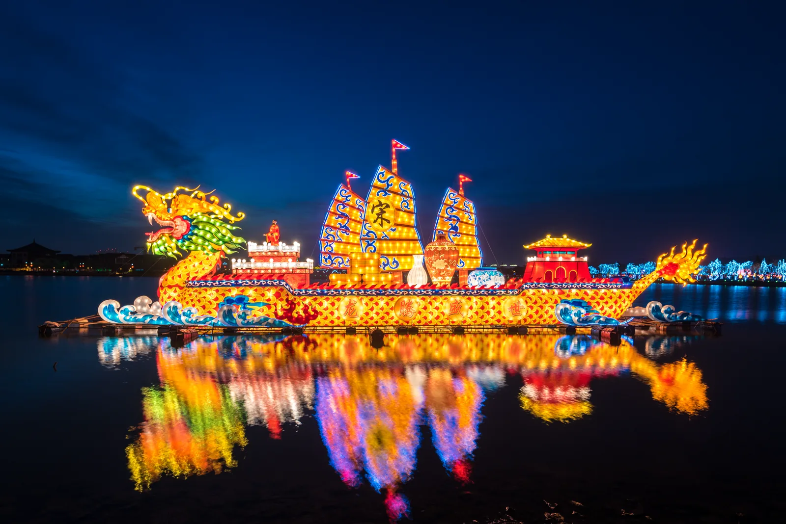 Large illuminated boat-form lantern display reflected in water at a Kaifeng lantern event