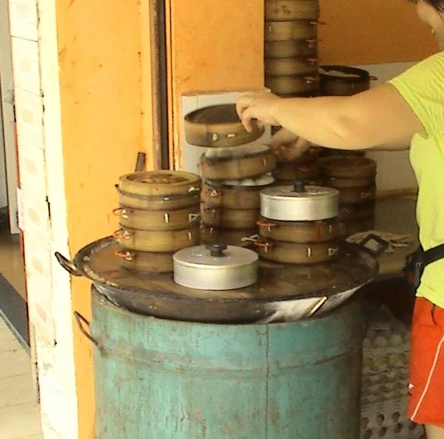 A baozi shop worker opening one of many bamboo steamers stacked on a large steam barrel in Haikou