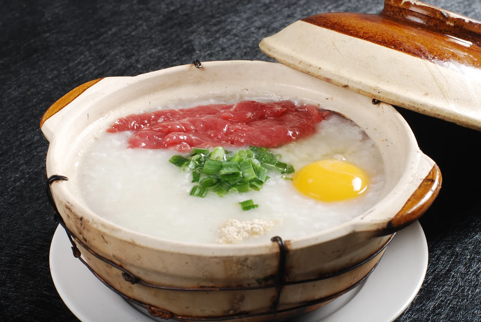 Chinese breakfast congee served in a clay vessel with beef egg and scallions