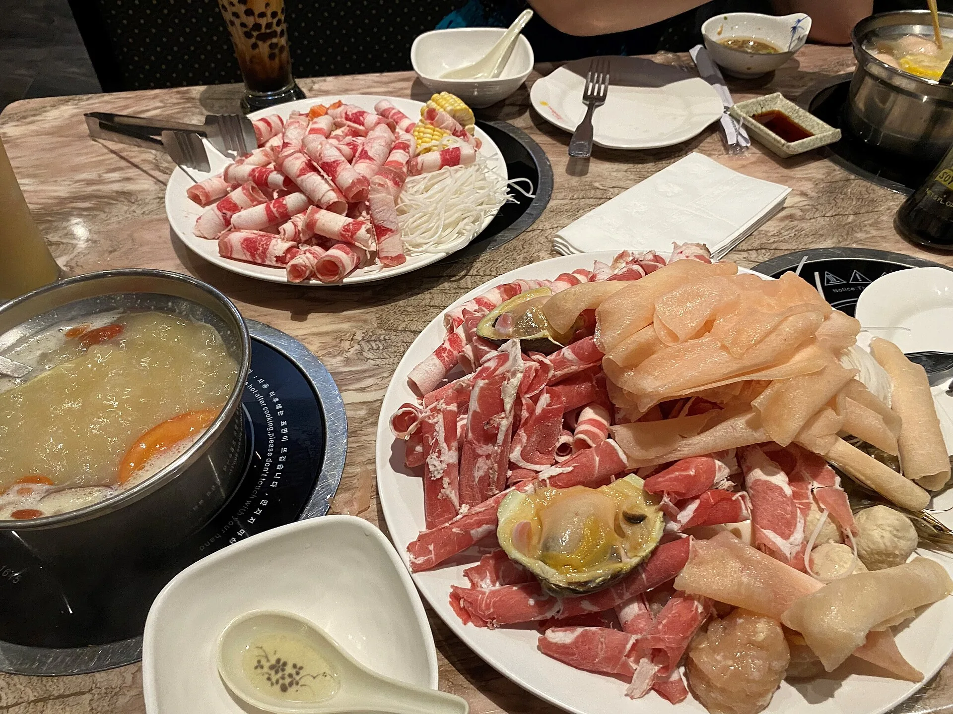Chinese food shared around a table with hot pot, vegetables and sliced ingredients