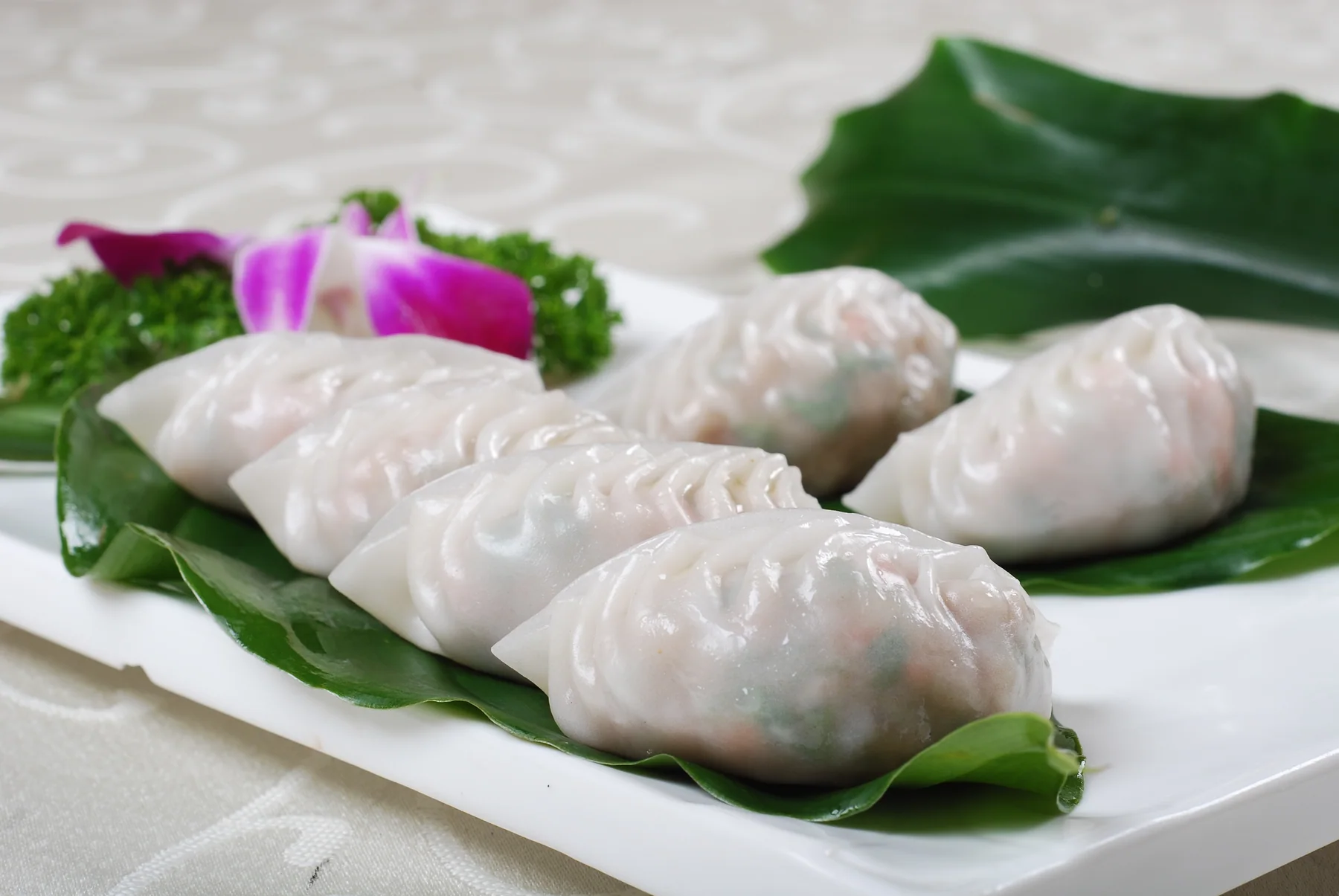 Six translucent crescent dumplings on green leaves with pink and green filling visible through the wrappers