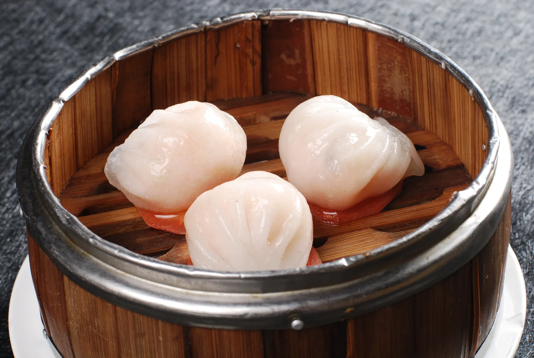 Three real har gow in a bamboo steamer with translucent wrappers revealing pale shrimp filling