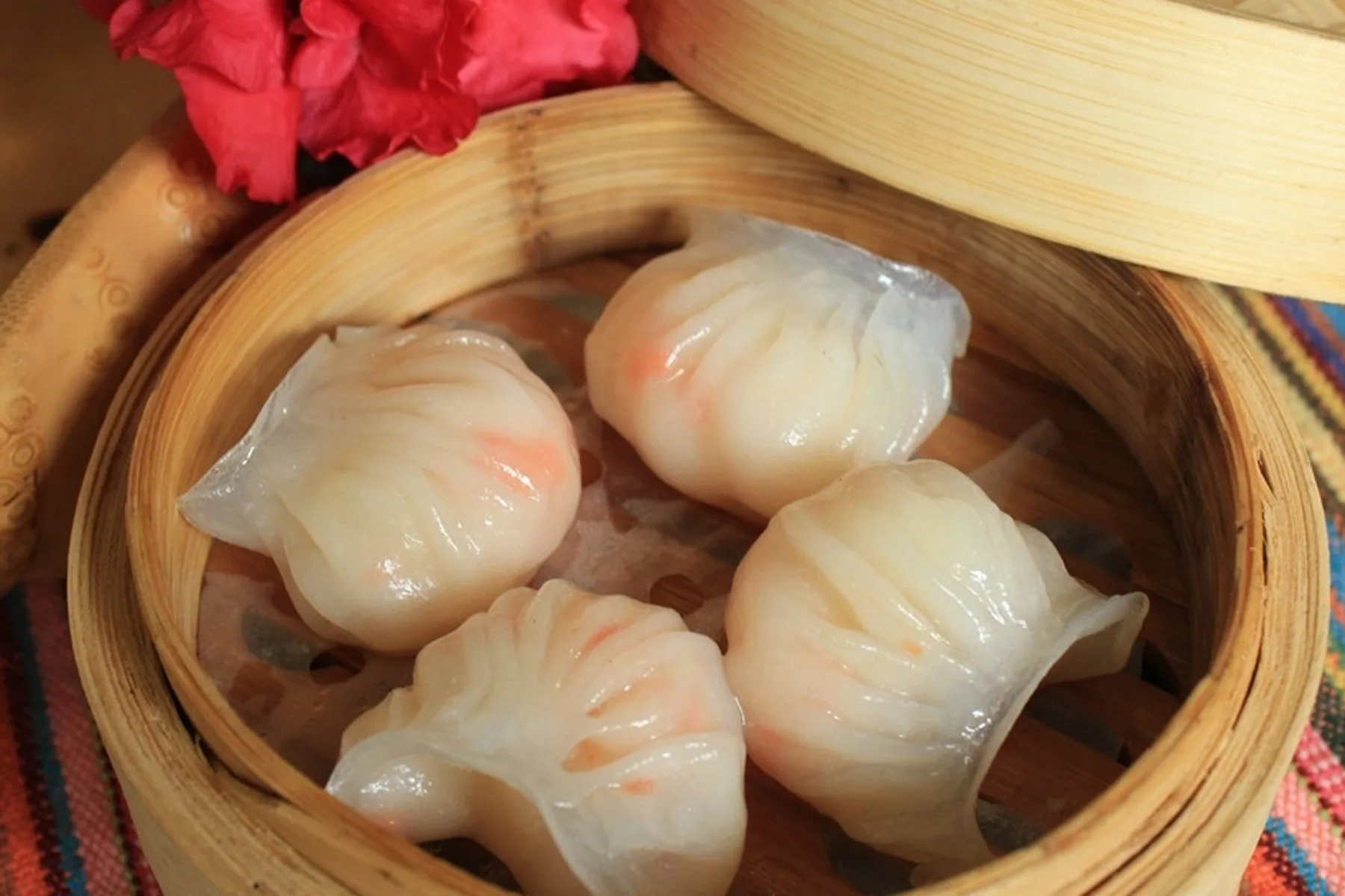 Four real har gow in a bamboo steamer showing different pleat depths, thin tails and visible shrimp color