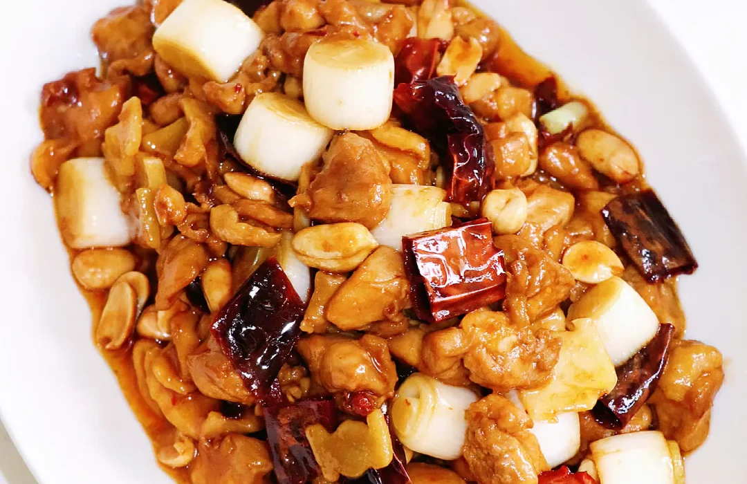 A home-cooked plate of Kung Pao chicken where diced chicken, dried chillies, peanuts and thick scallion sections remain individually visible