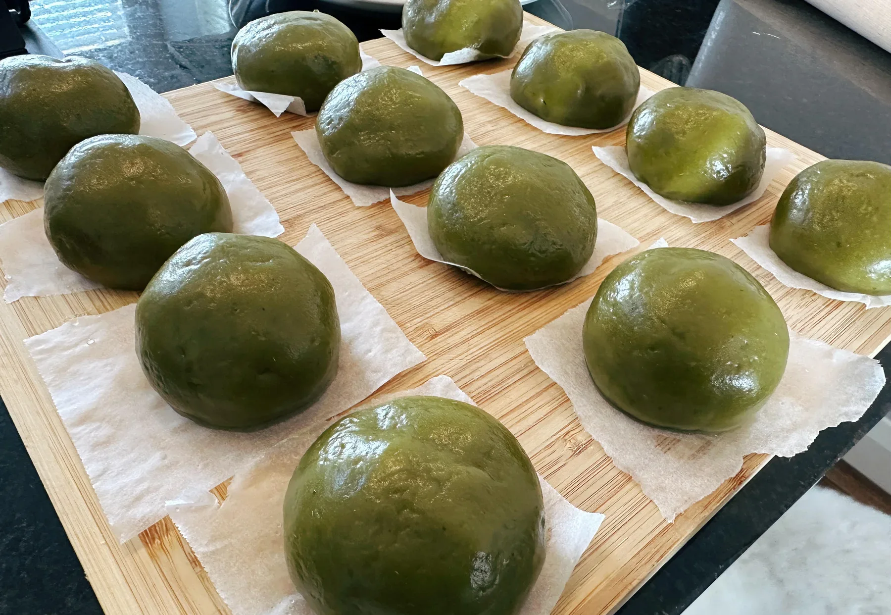 A tray of handmade glossy green qingtuan resting on individual paper squares