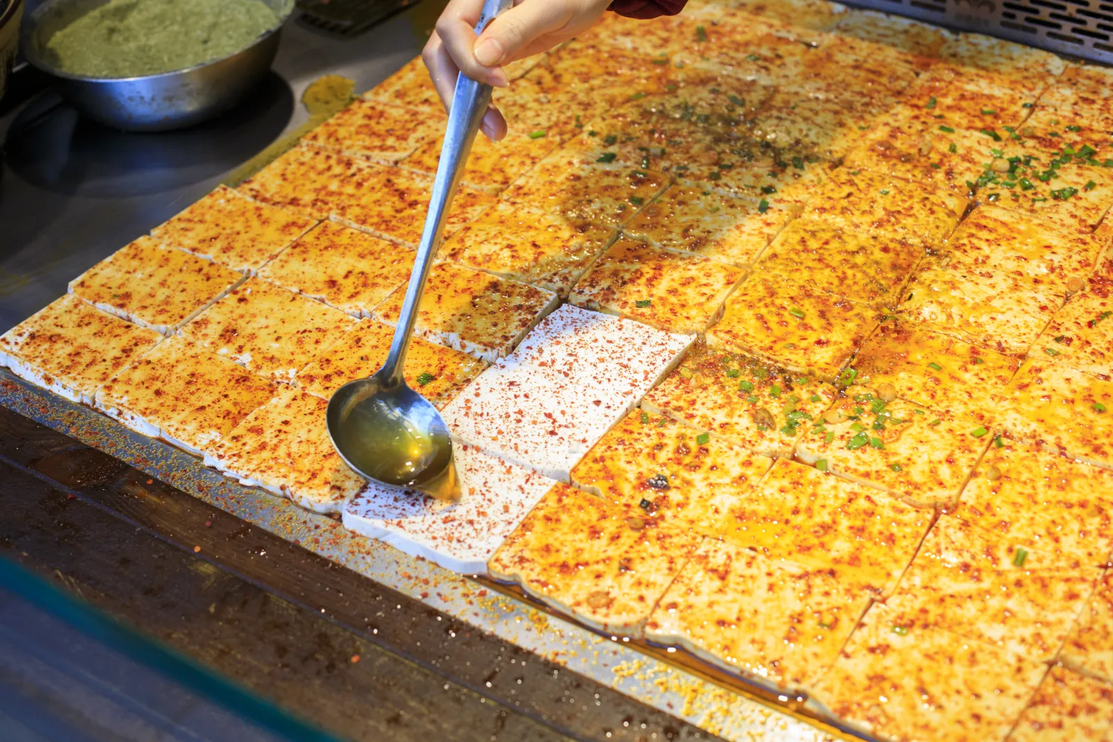 Squares of tofu brushed with oil and chili seasoning at a street-food counter