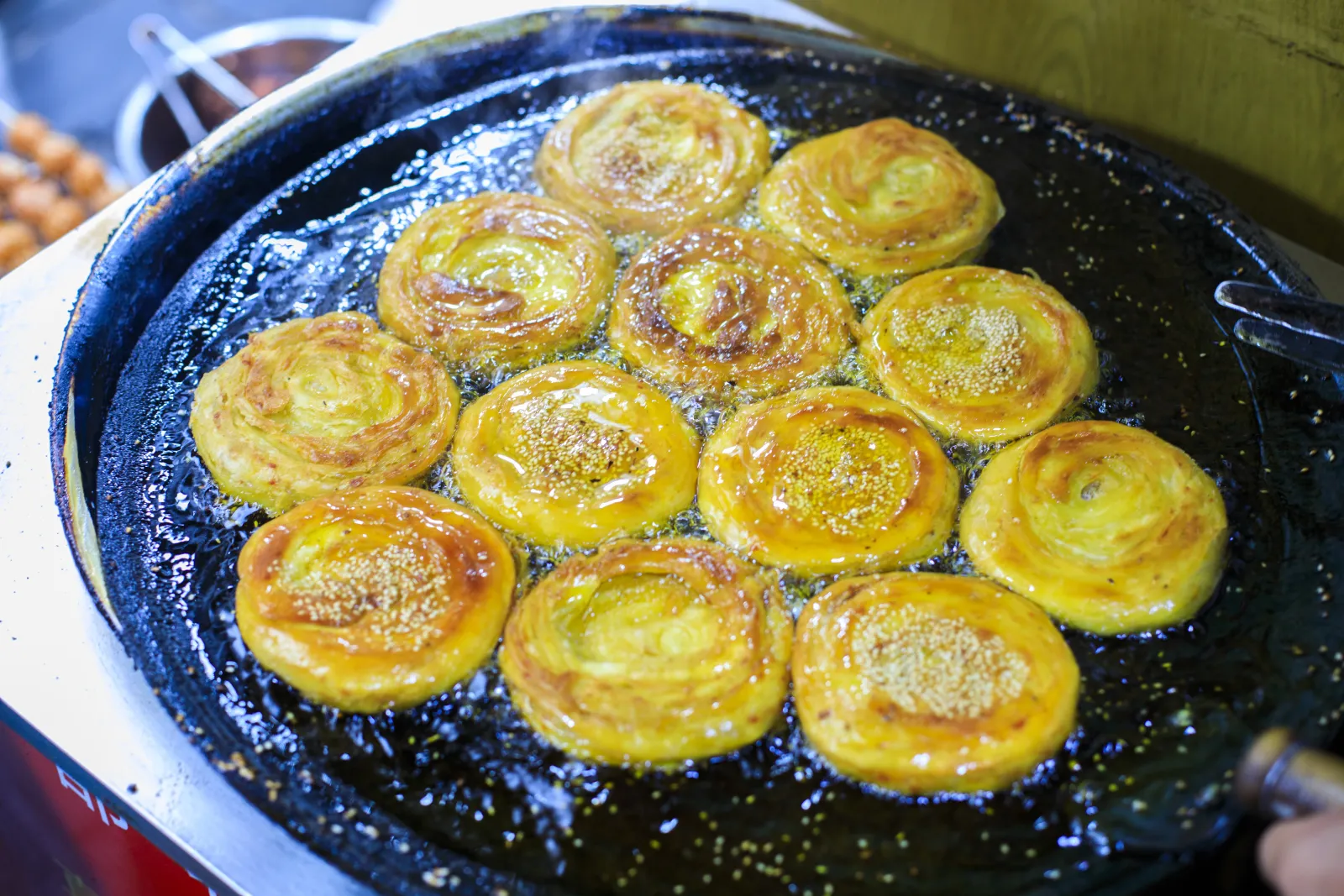 Round layered pastries frying on a wide iron pan at a Chengdu snack stall