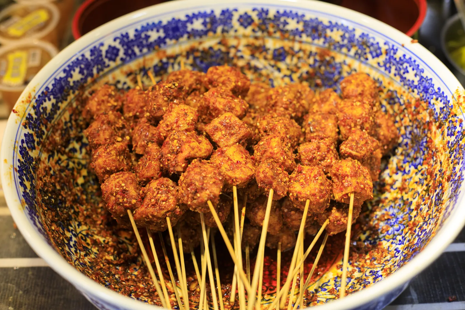 Skewered Chengdu street snacks coated with red chili and aromatic spices in a blue-and-white bowl