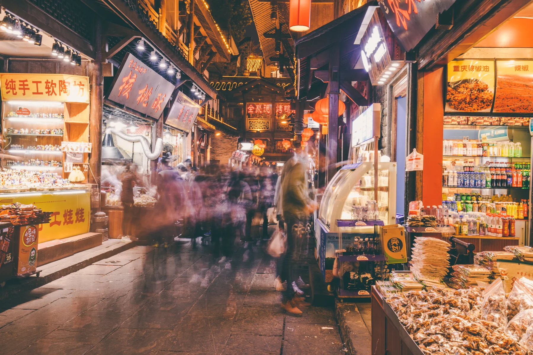 A narrow Chongqing food street busy with evening diners and illuminated signs