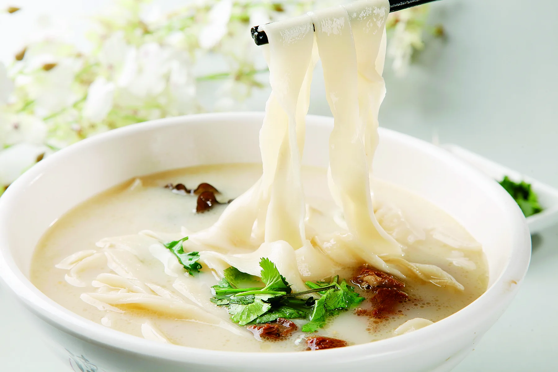 A bowl of Henan huimian with broad hand-stretched noodles, broth, mushrooms and greens