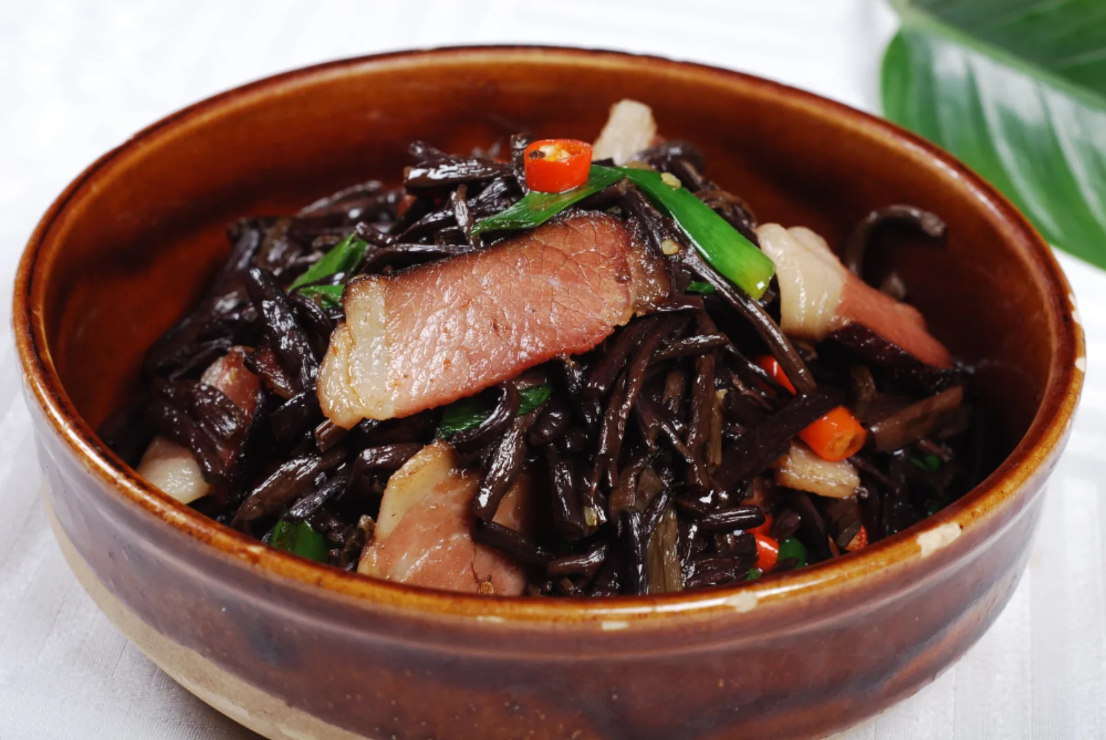 Hunan smoked pork stir-fried with dark bracken in a brown ceramic bowl