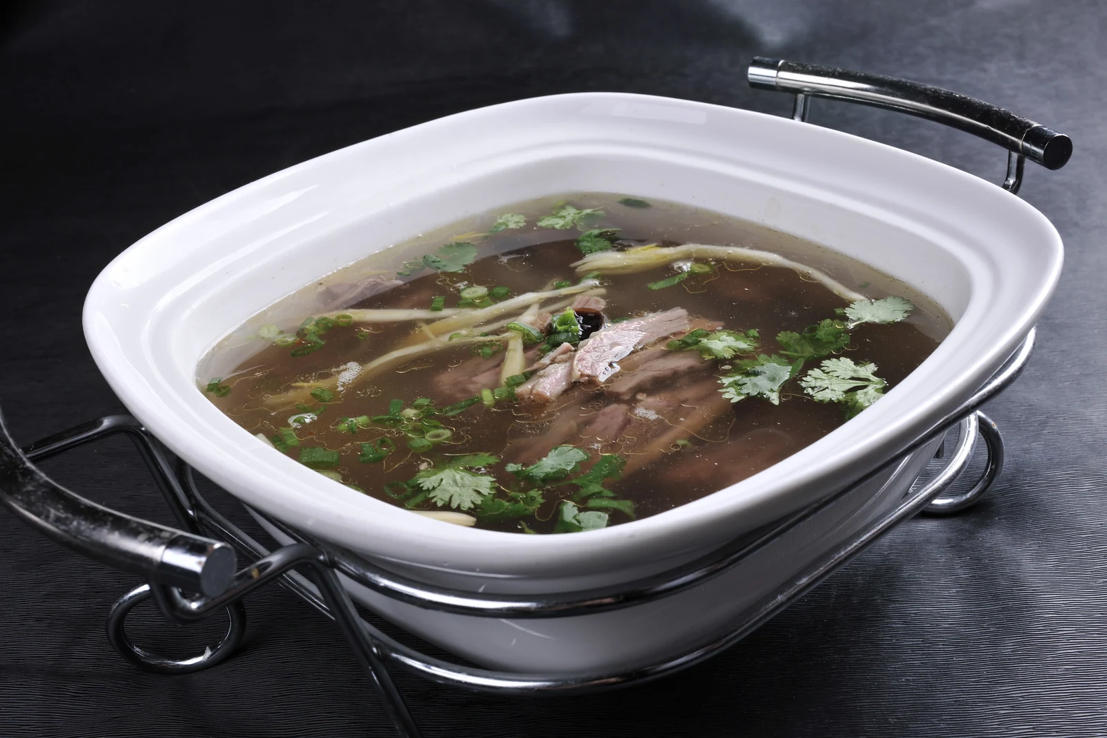 A Henan lamb soup with sliced meat and fresh herbs in a clear broth