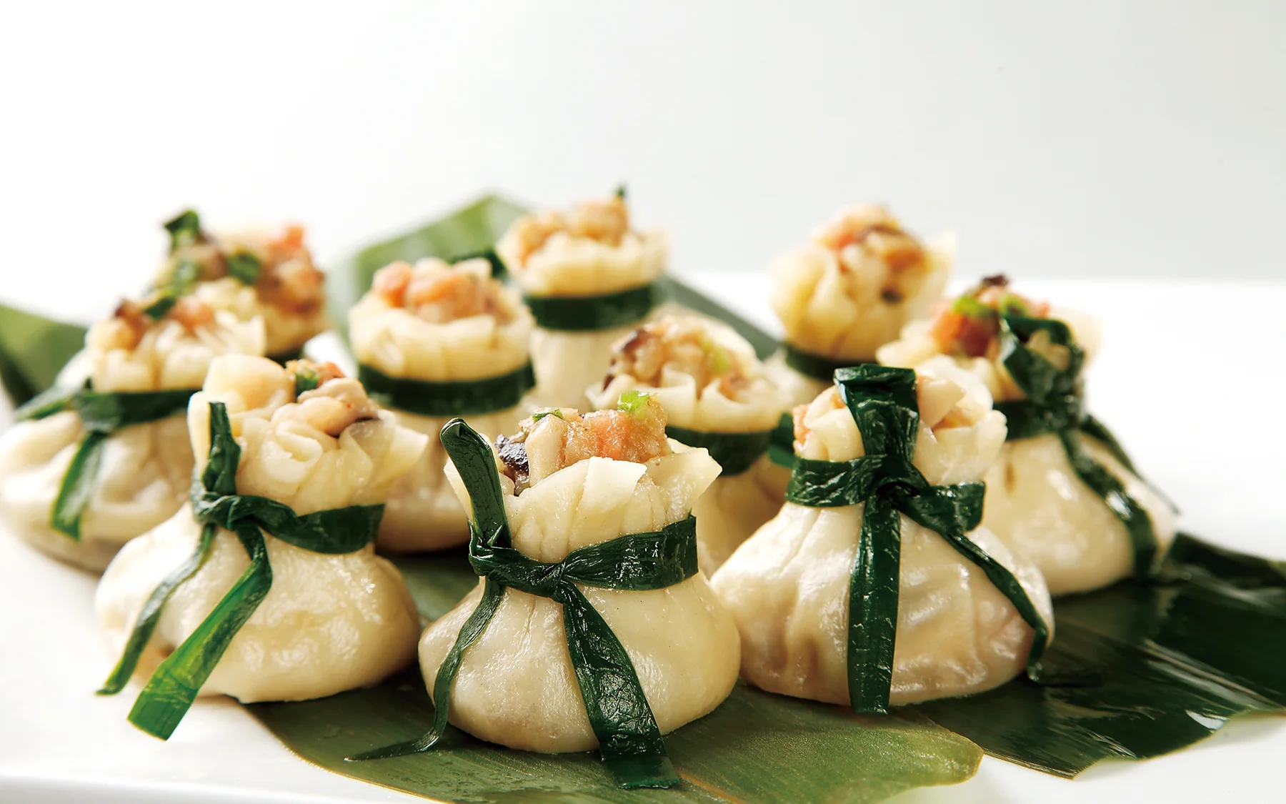Open-topped shaomai tied with green leaves, making wrapper, filling size and moisture visible at the morning-tea table
