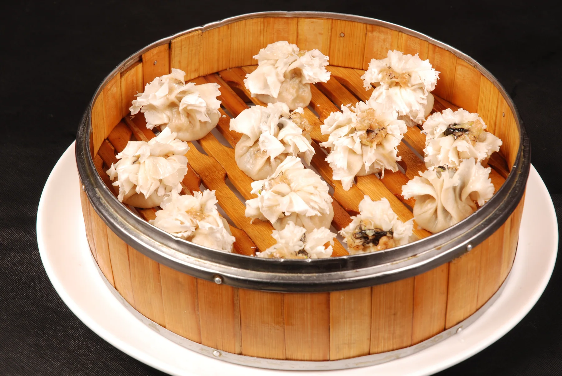 Flower-topped shaomai spread across a bamboo steamer with pale shredded wrapper collars
