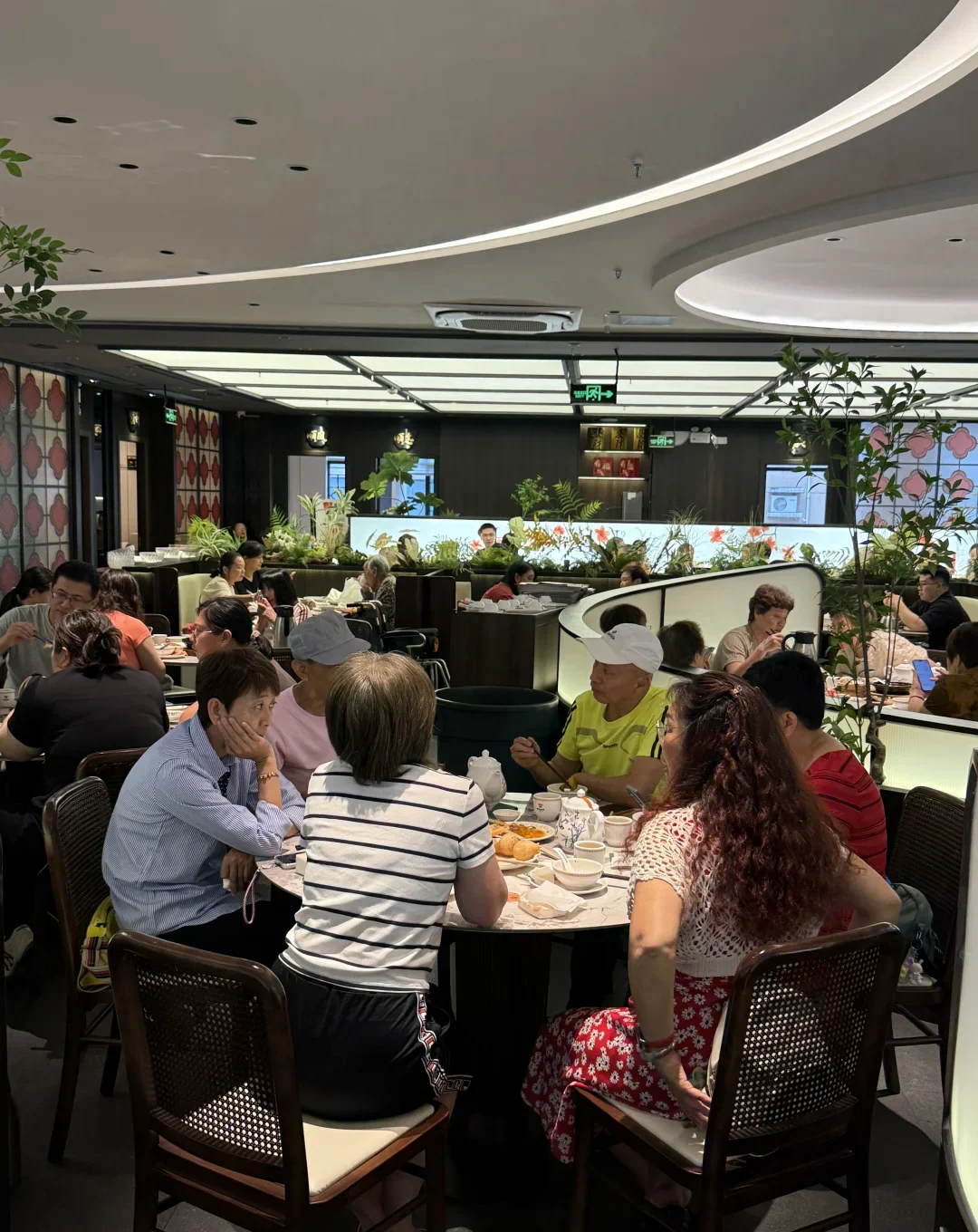 Groups of diners talk and eat around round tables in a busy contemporary Guangzhou yum-cha dining room