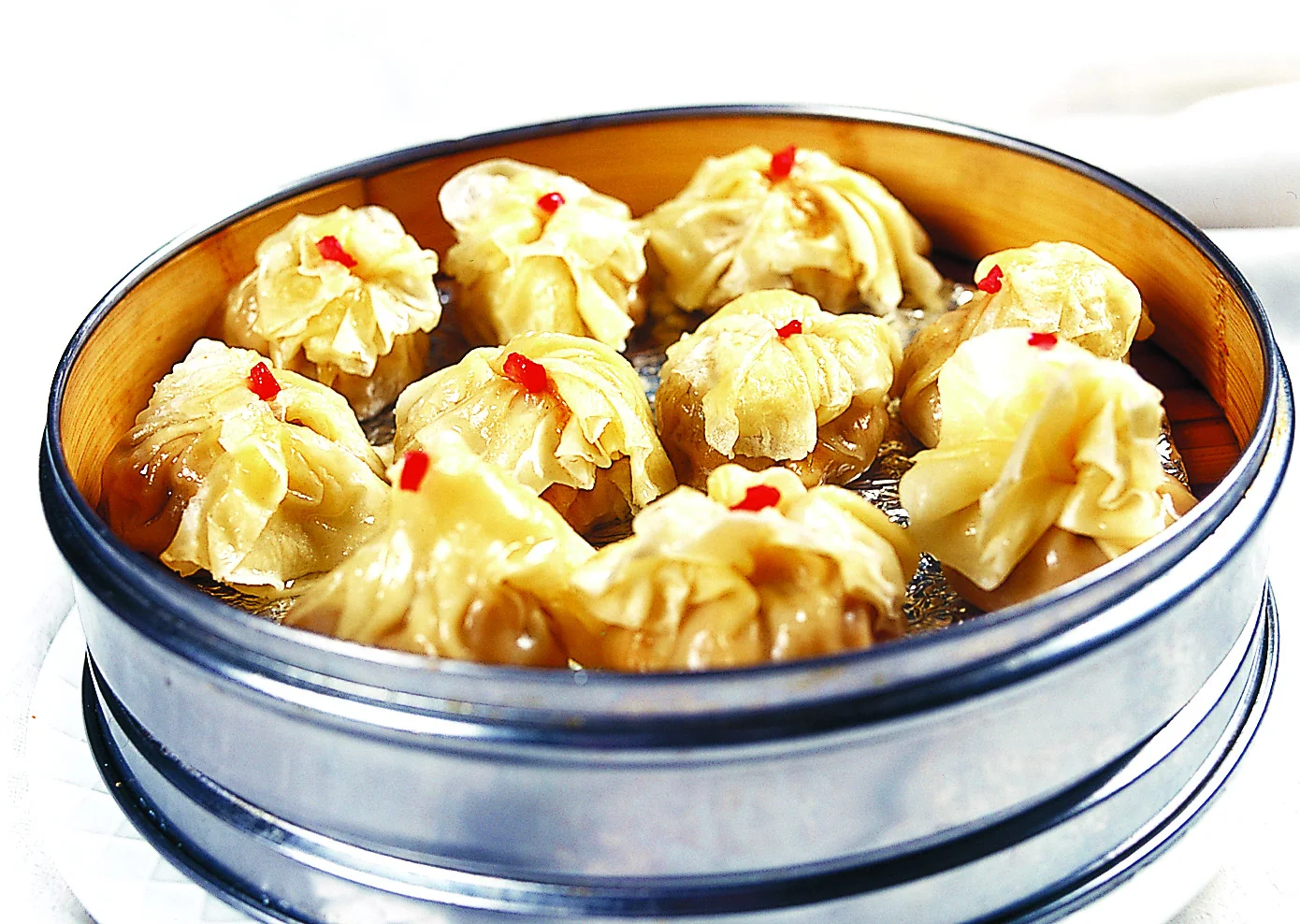 A metal steamer filled with tall shaomai whose pale wrapper caps sit over glossy brown sides