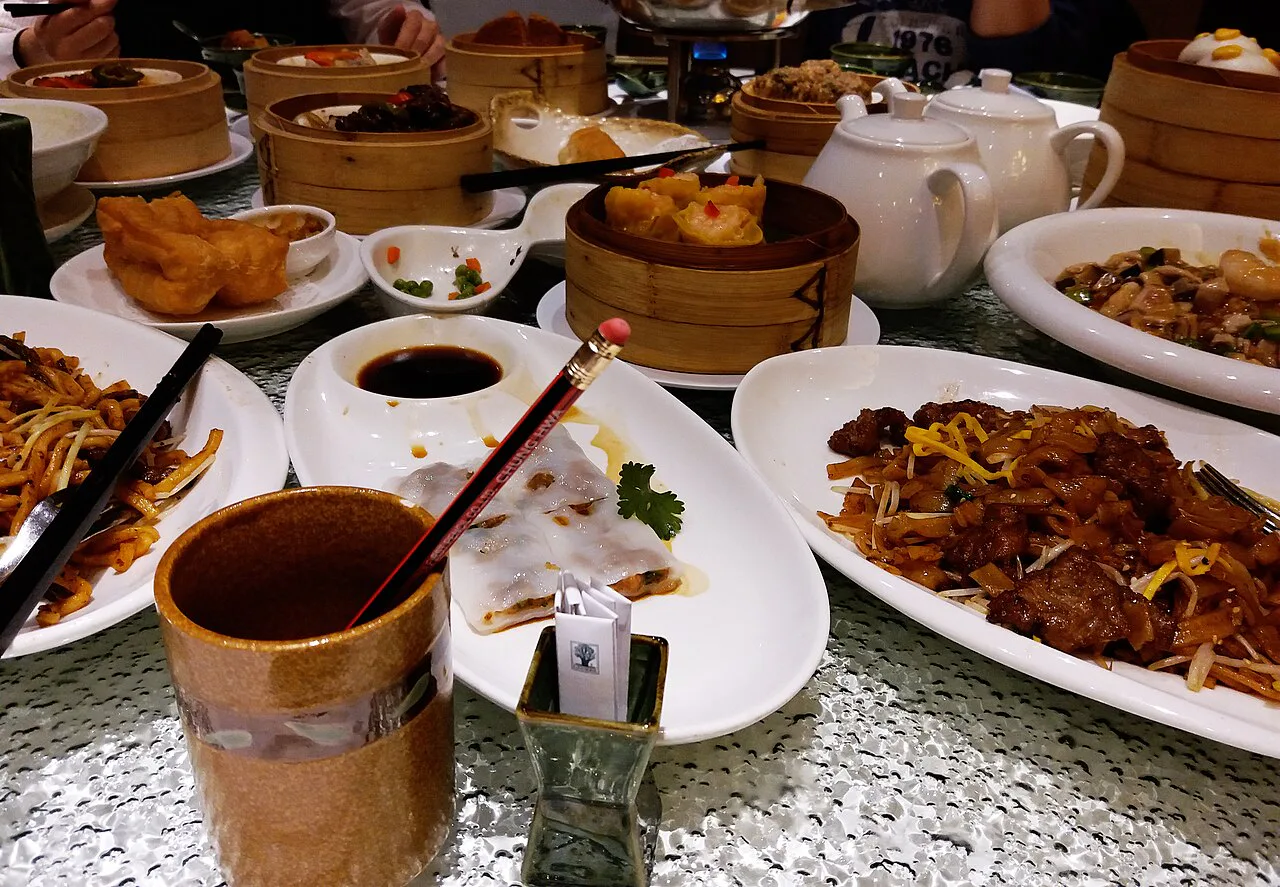 A real yum cha table with bamboo steamers, tea, shared dishes and diners reaching across the meal