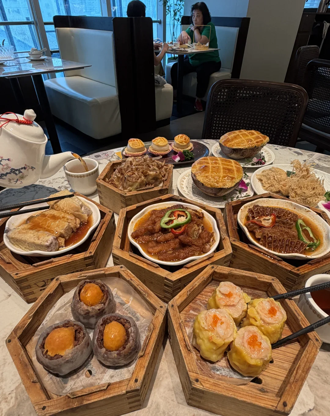 A Guangzhou yum-cha table crowded with bamboo steamers, tea, savory dishes and two baskets of open-topped shaomai
