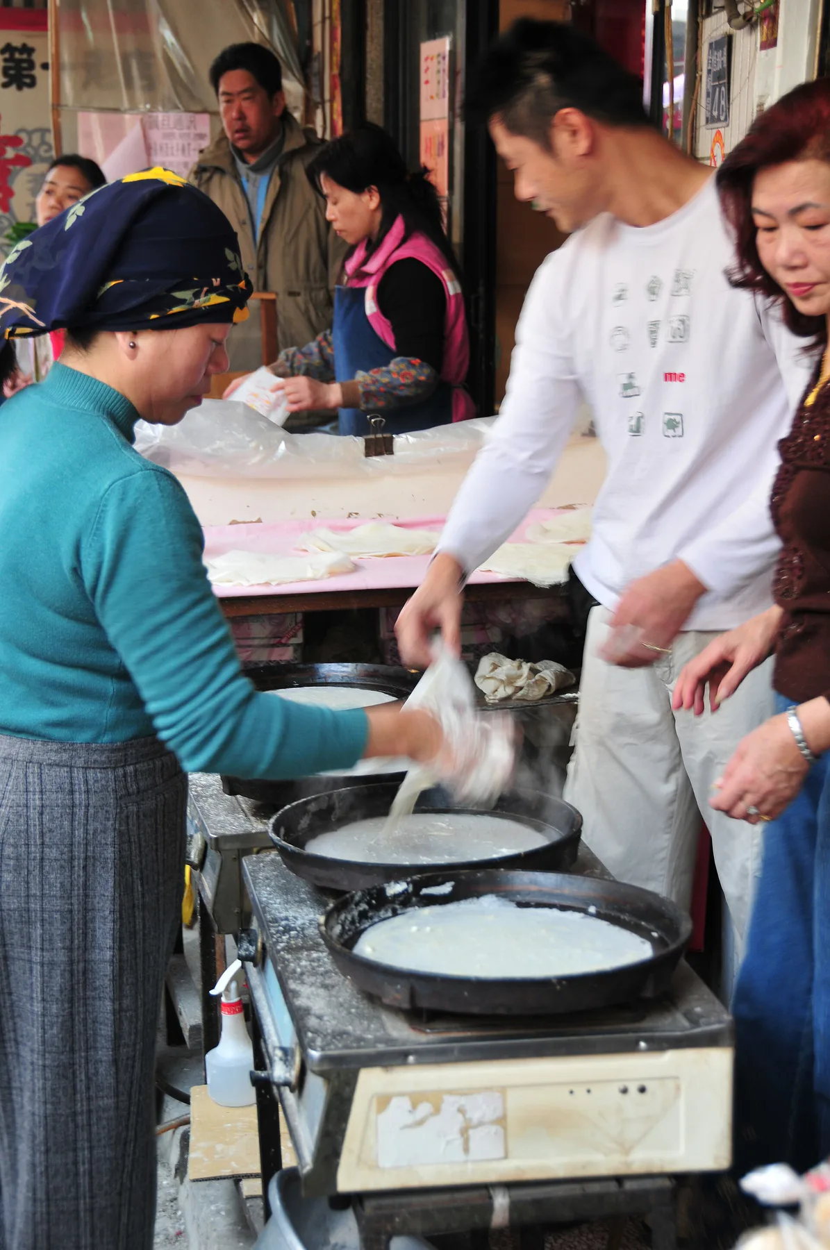 A Kinmen street vendor spreads popiah-style wrapper batter across round hot plates as customers gather at the stall