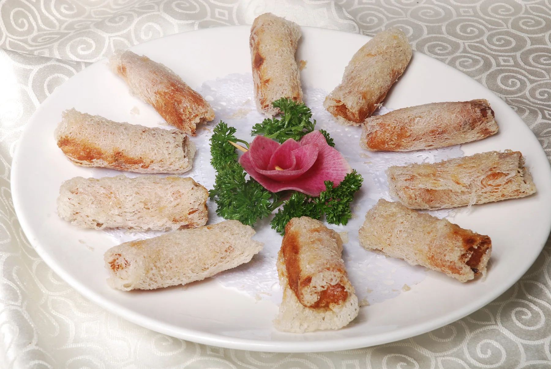 Short fried rolls with a fine net-like wrapper arranged around a plate