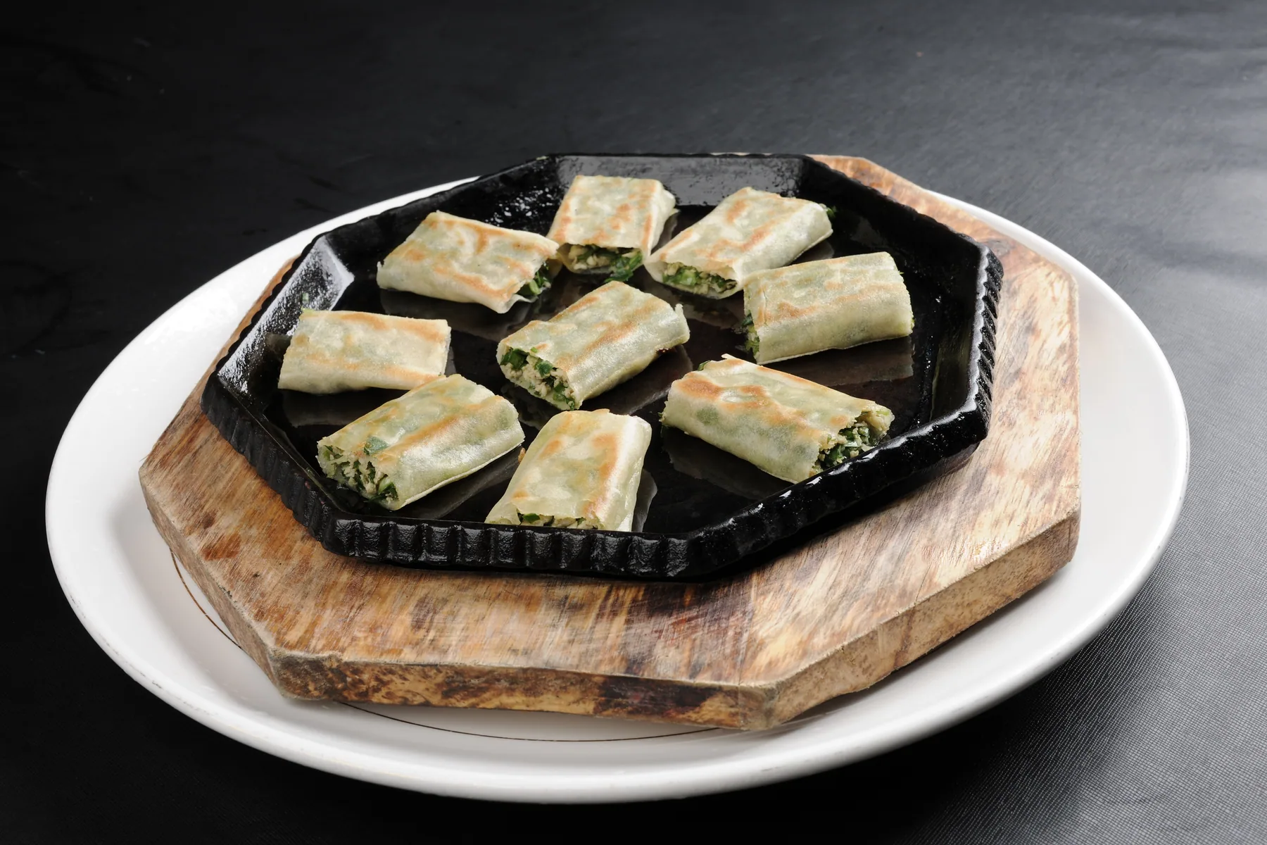 Pan-fried spring-roll pieces on a hot plate exposing a moist green vegetable filling and lightly browned wrapper