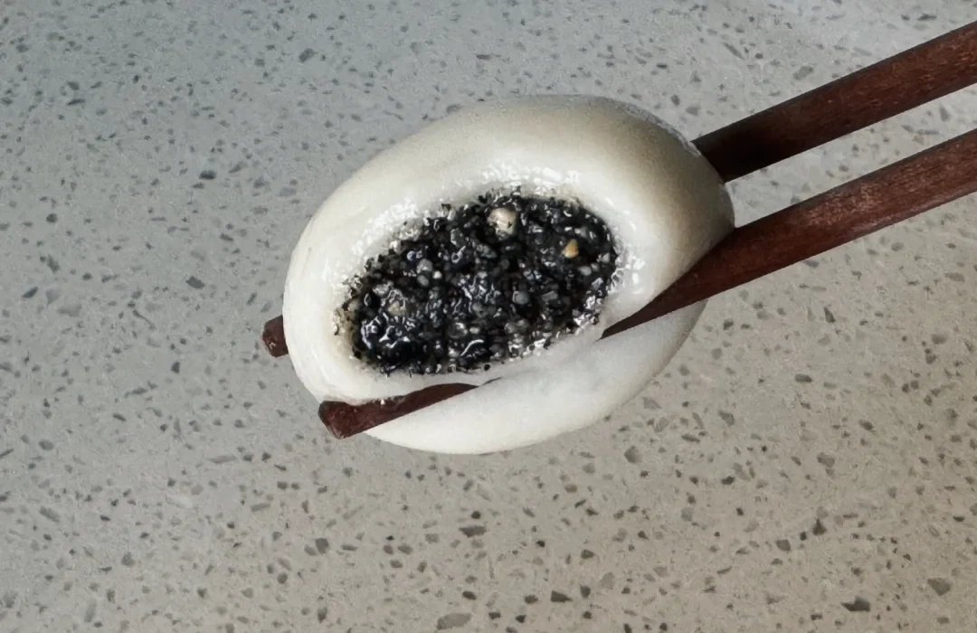 A freshly cooked black-sesame tangyuan cut open to show a thin white wrapper and textured filling