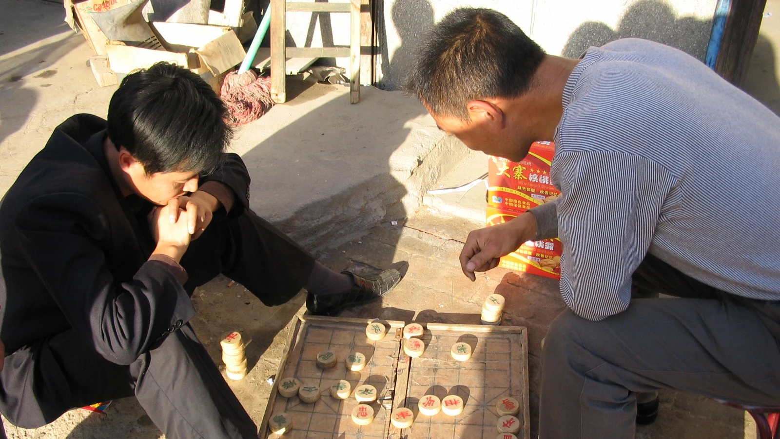 Two men leaning over a well-used xiangqi board during an outdoor game in Datong