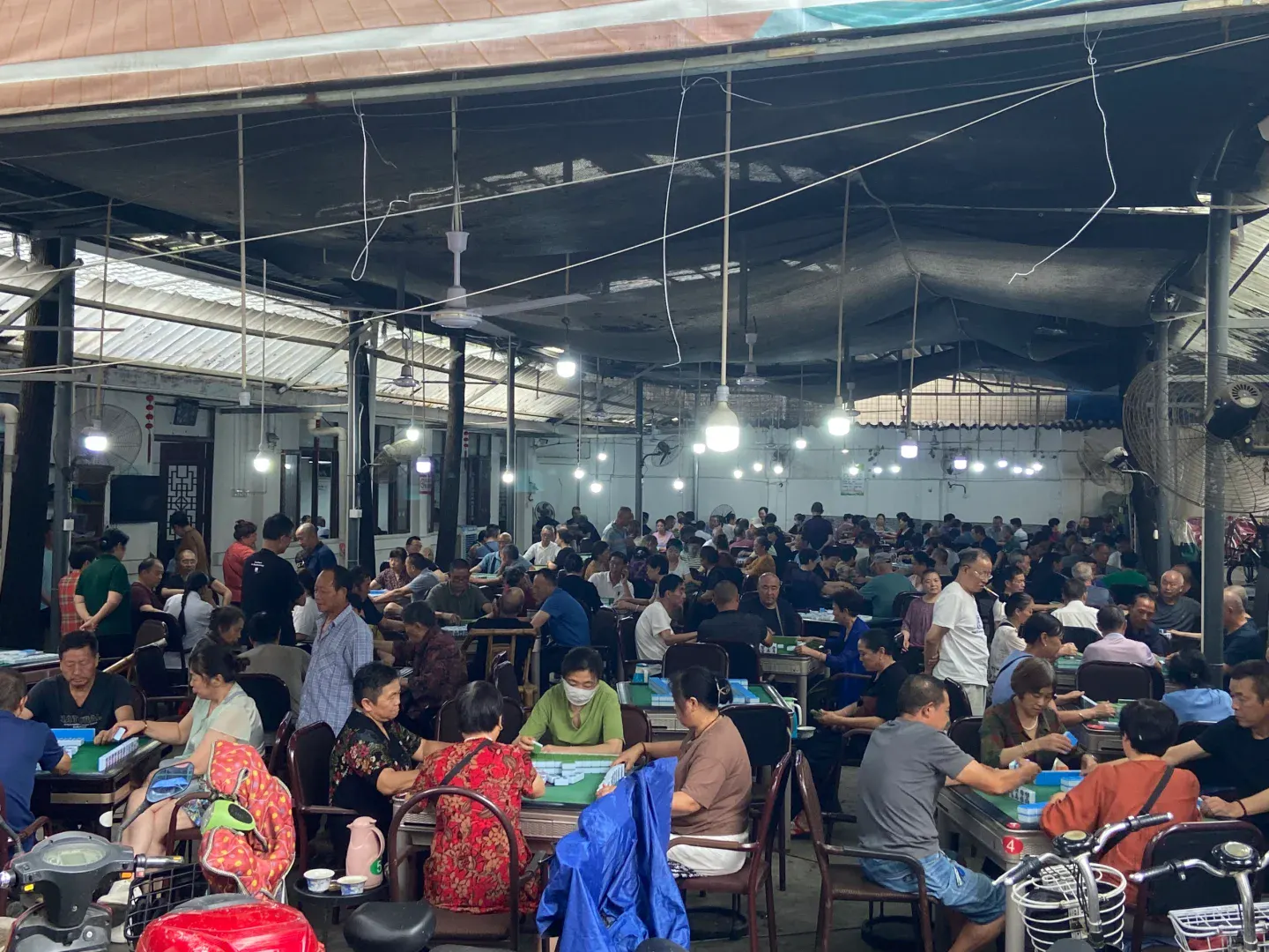 A crowded late-afternoon community mahjong hall in Chengdu with many tables playing at once