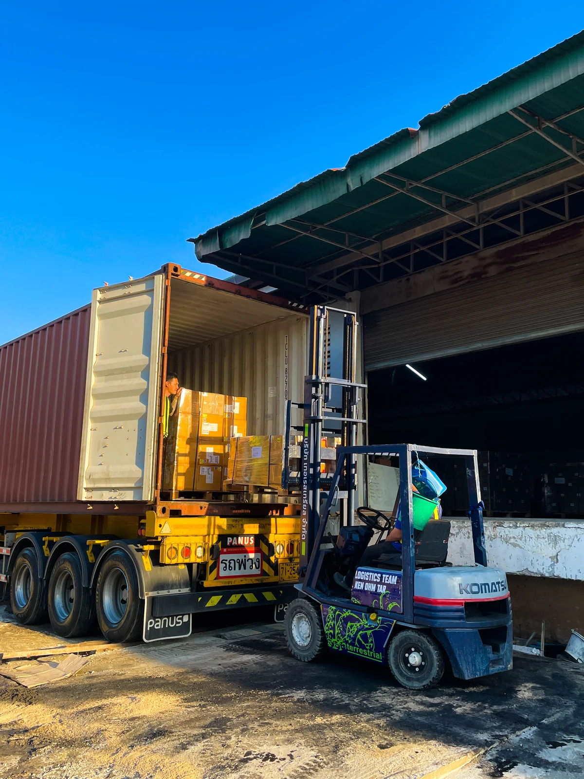 A warehouse worker uses a forklift to move palletized cartons into a shipping container
