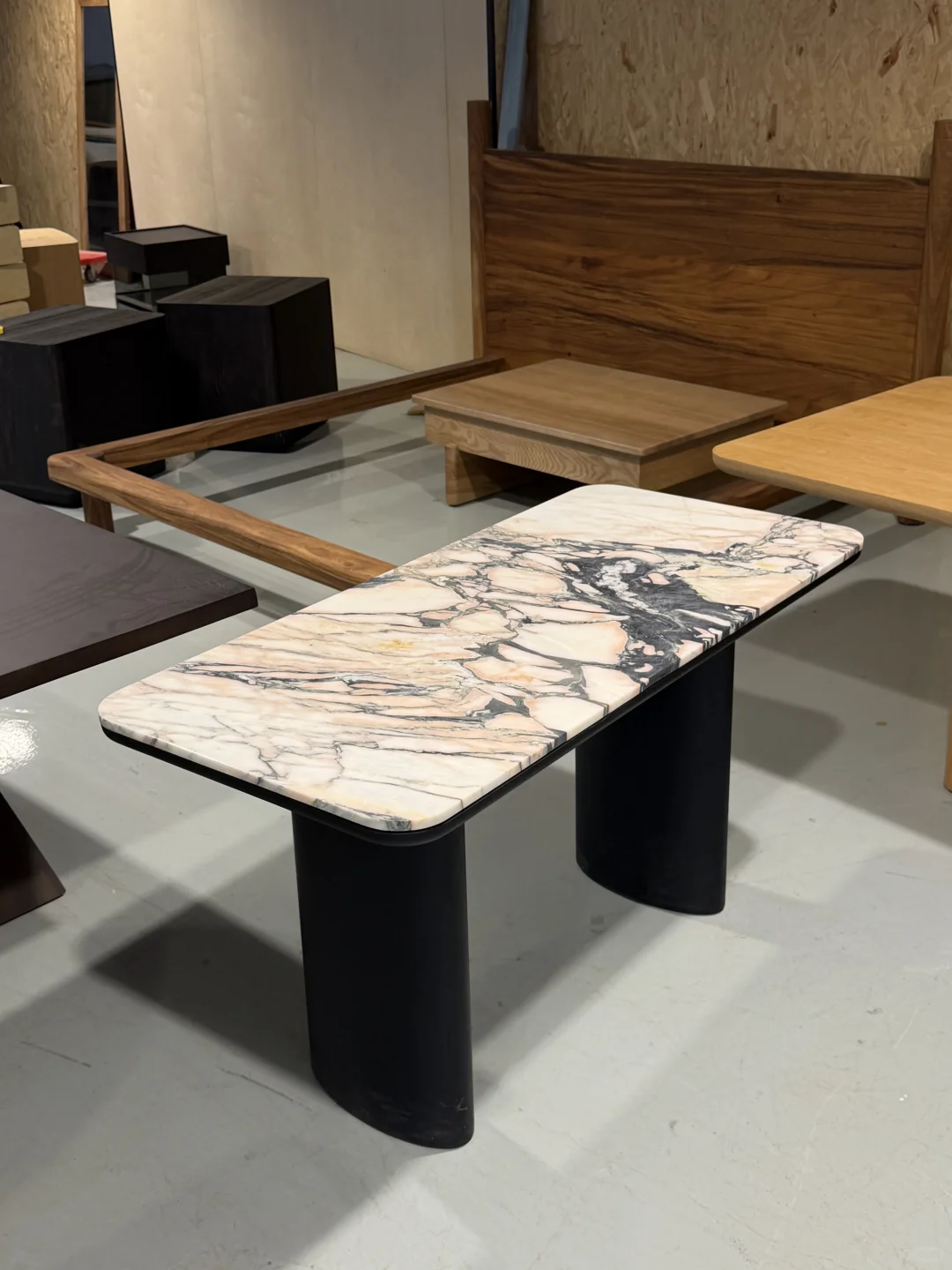A stone-pattern tabletop on dark curved legs sits among wood furniture samples in a showroom