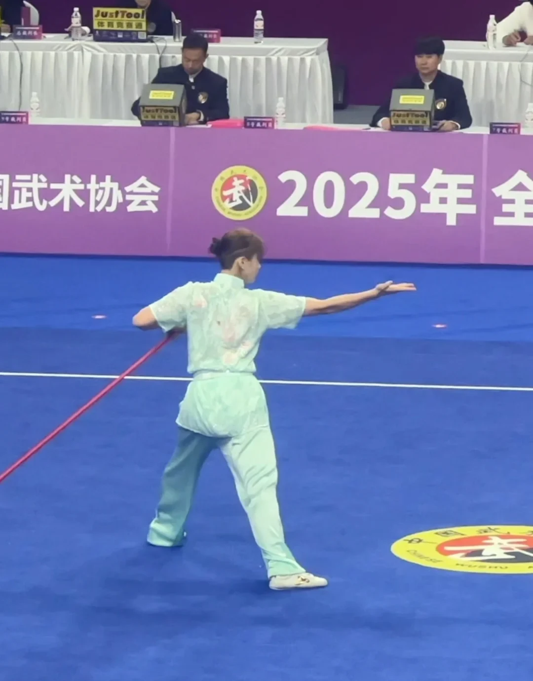 Qiangshu athlete carrying the red shaft through a low competition stance at the 2025 national wushu taolu championship