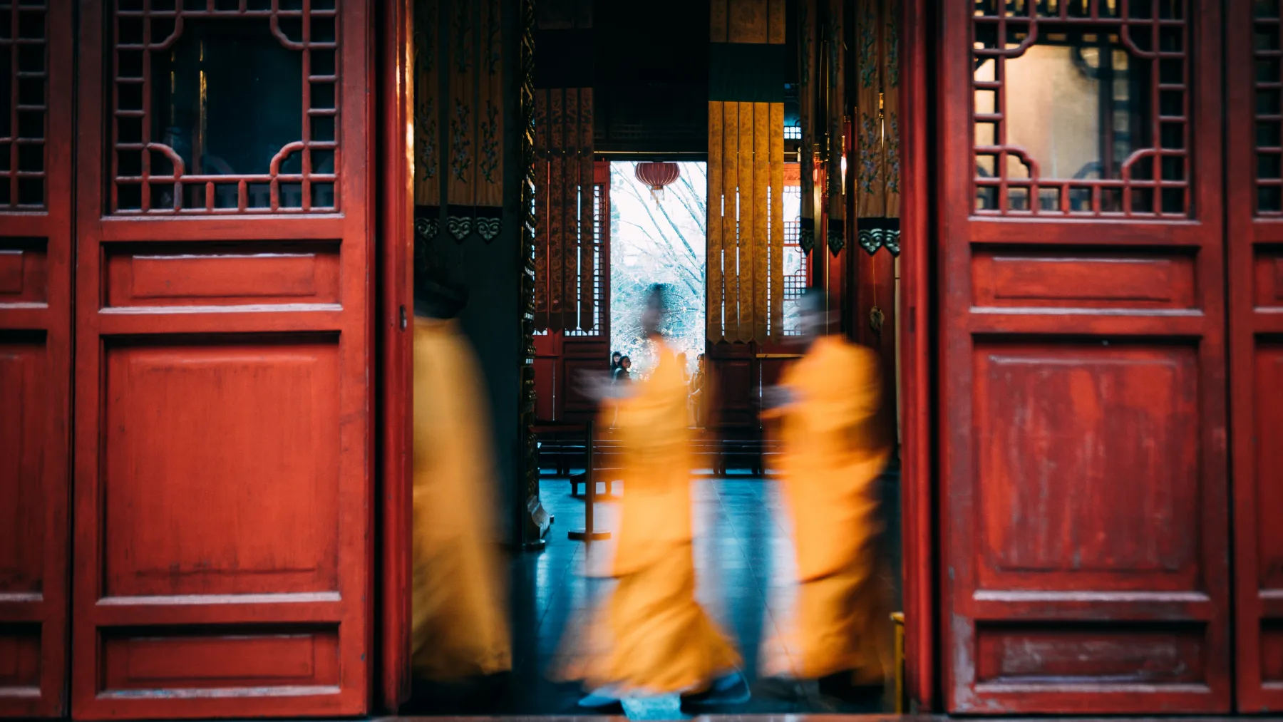 Blurred saffron-robed monks moving through a red-doored courtyard at Shaolin Temple