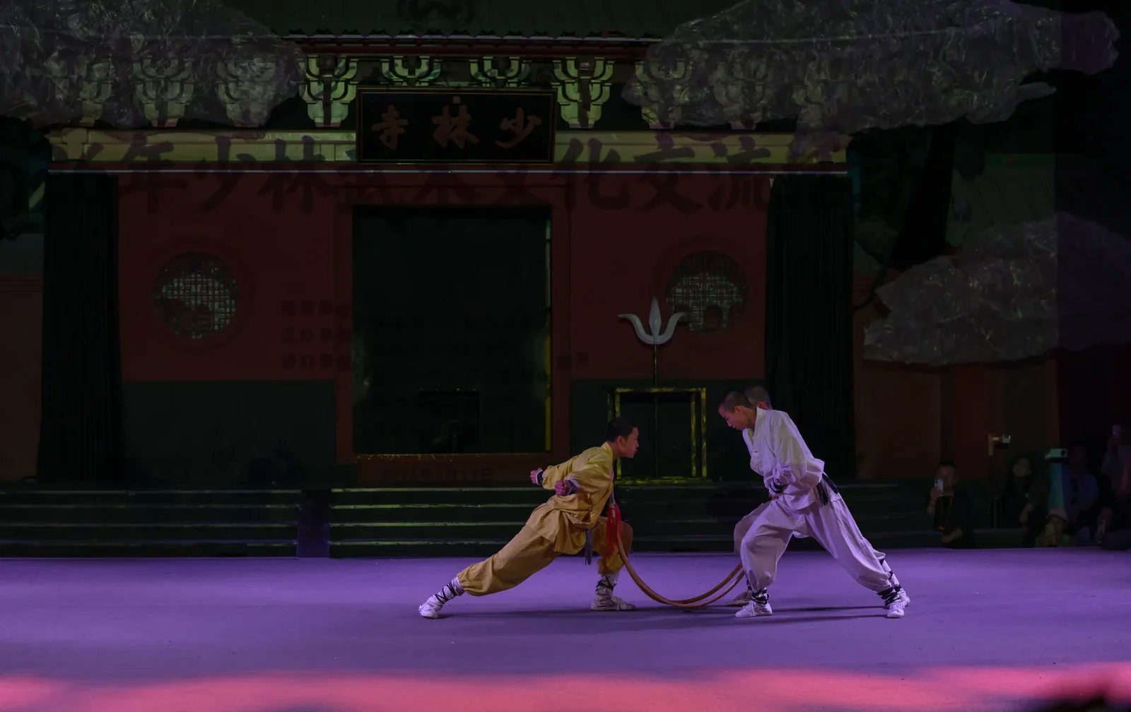 Two Shaolin performers testing stance and timing through a shared rope on a public stage