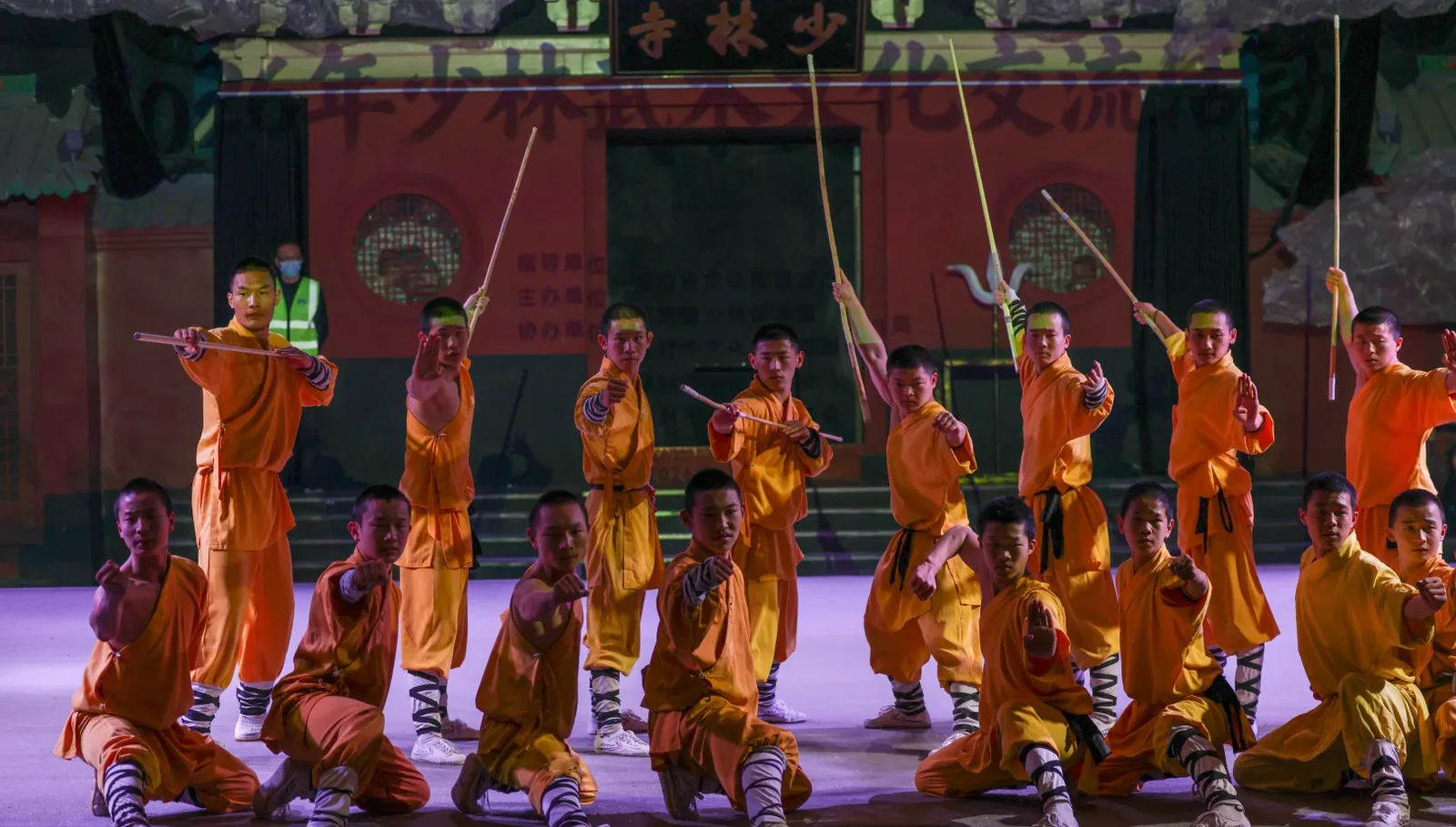 Shaolin performers holding staffs in a bounded public-stage formation