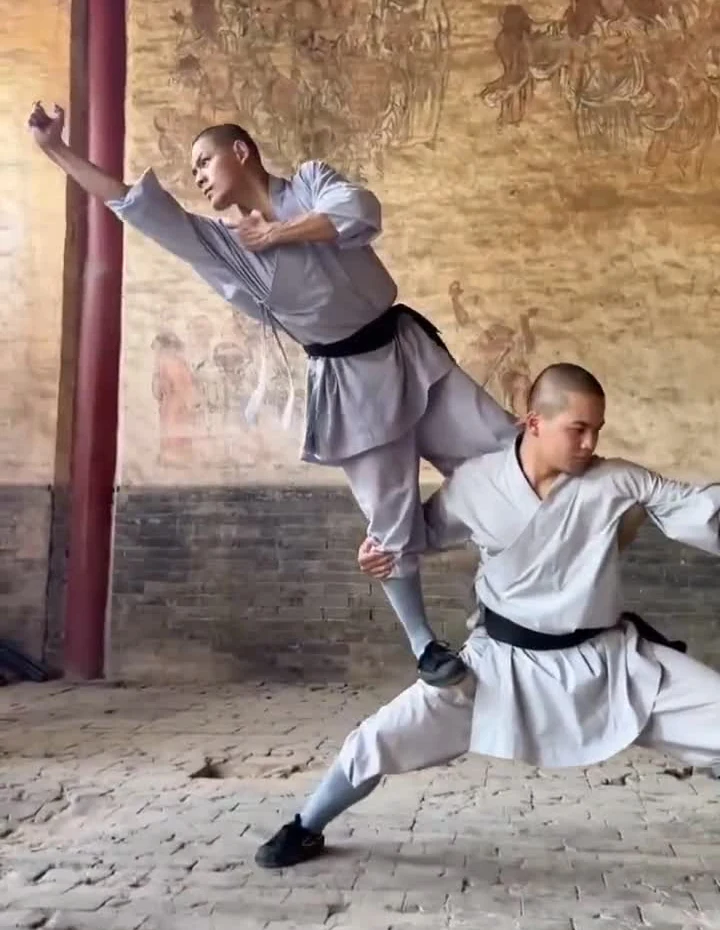 Two Shaolin performers holding an off-centre paired balance inside a temple corridor
