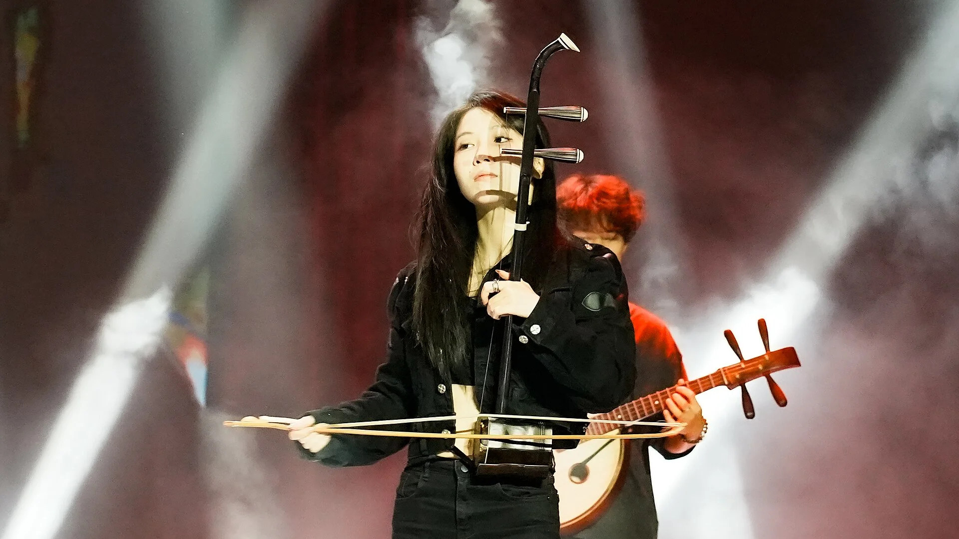 An erhu player draws the bow horizontally across the two-string instrument during a contemporary stage performance