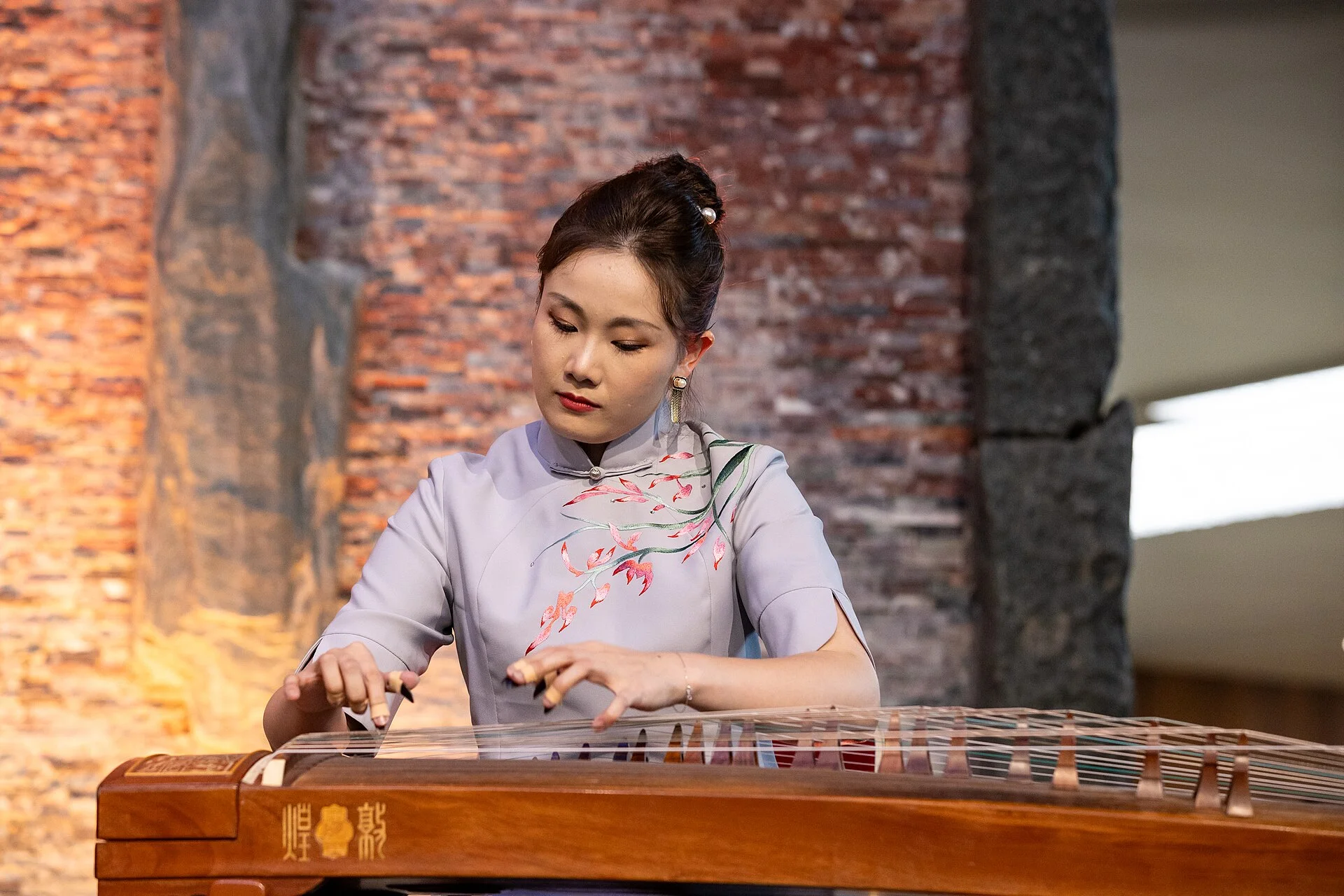 A guzheng performer using both hands across the strings and movable bridges at a WIPO cultural event