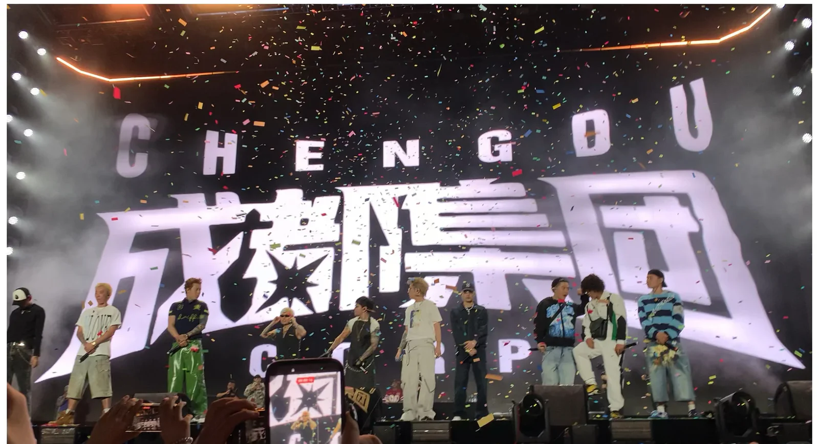 Multiple Chengdu rap performers standing across one festival stage beneath falling confetti