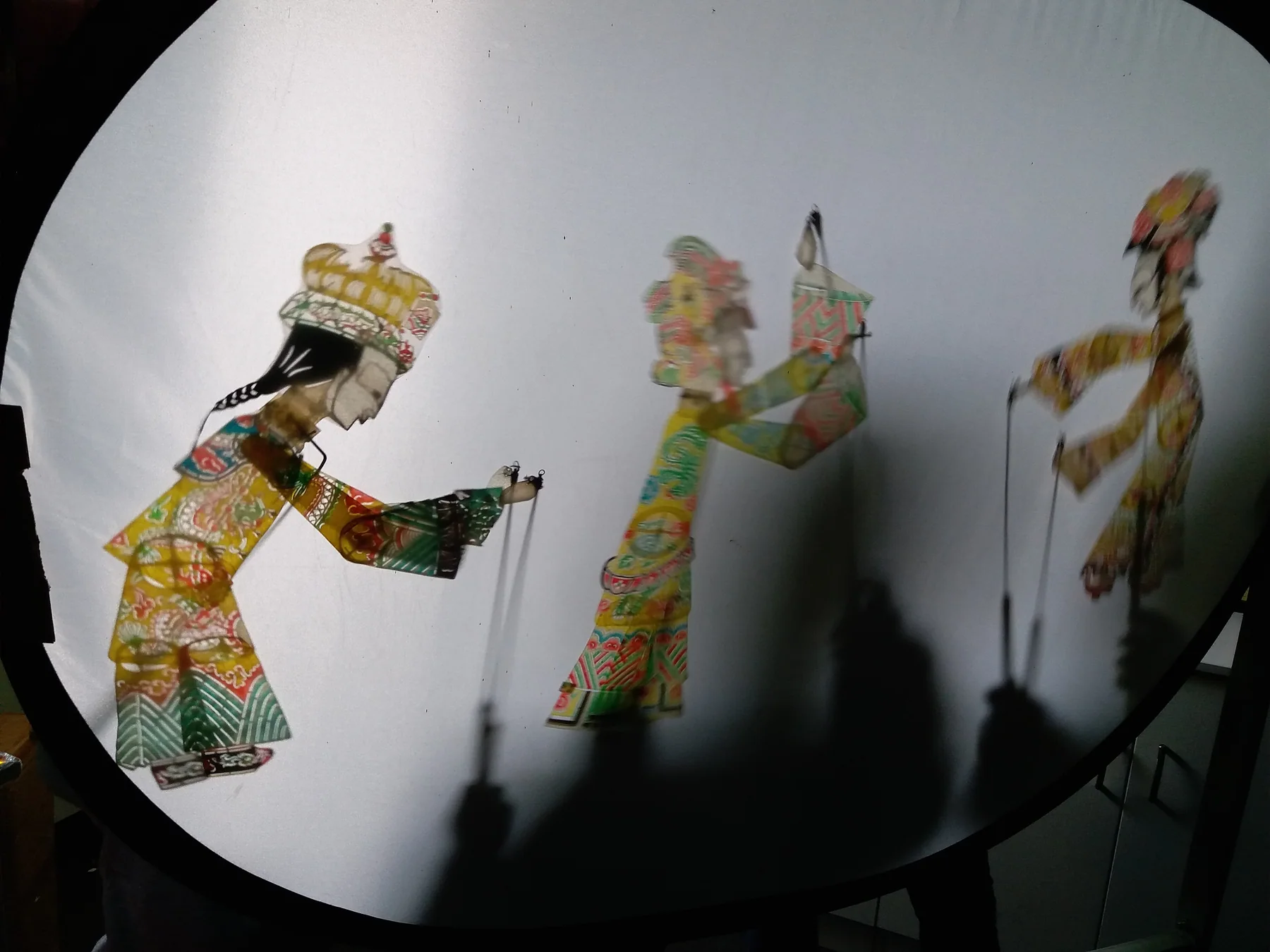 Colorful articulated figures projected across a lit Chinese shadow-puppetry screen