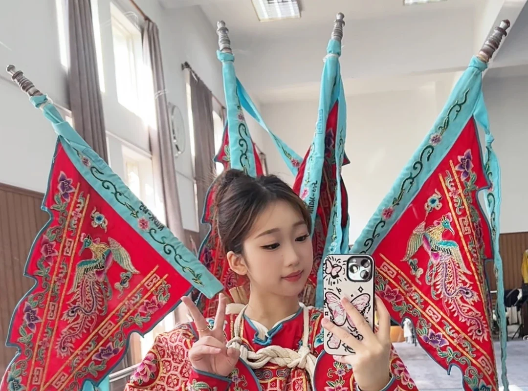A young Peking Opera learner wearing a red embroidered kao with four back flags during costume practice
